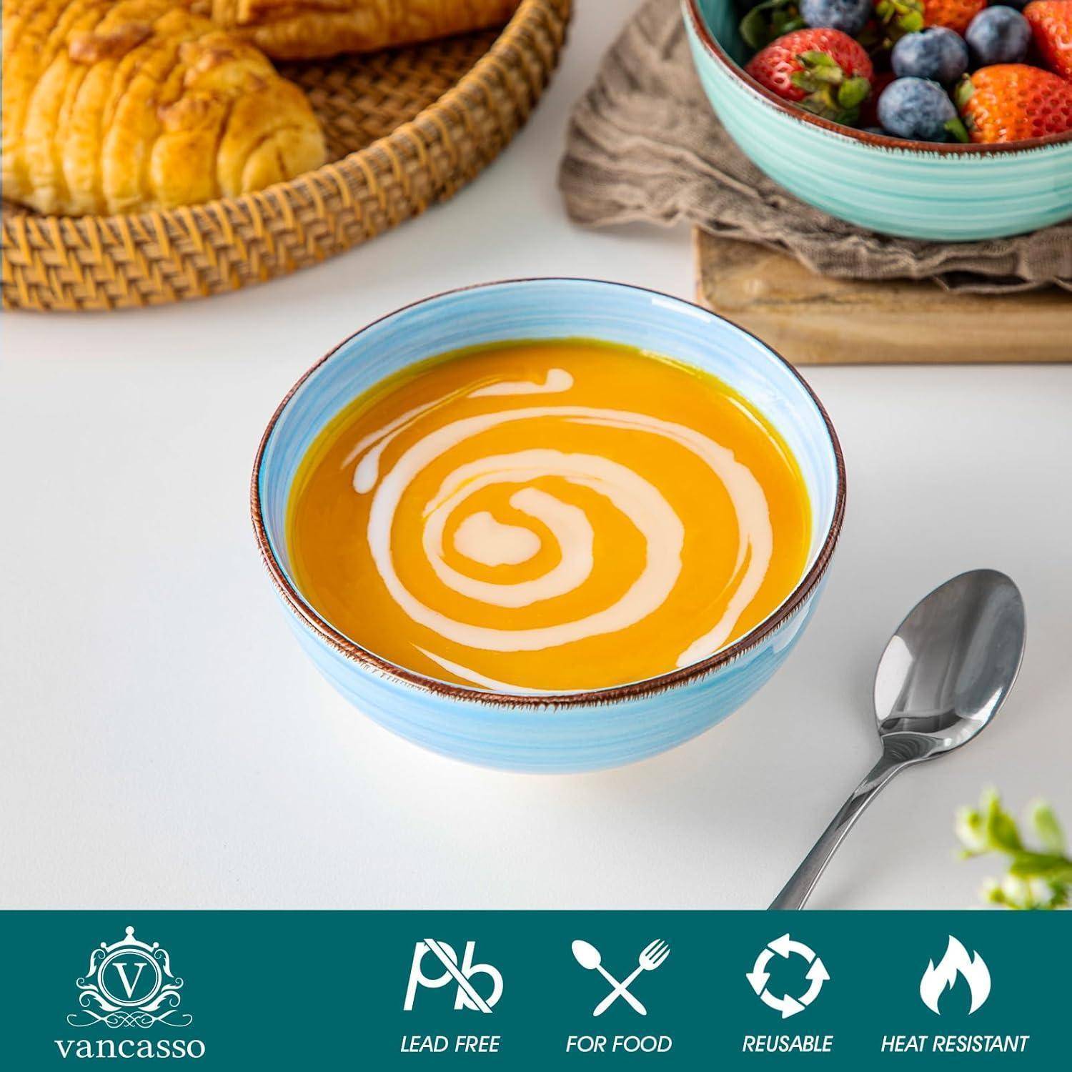 Eine Wirbel aus cremiger, gelber Suppe in einer Schüssel mit einem Löffel daneben; Croissants und eine Schüssel mit Beeren im Hintergrund.
