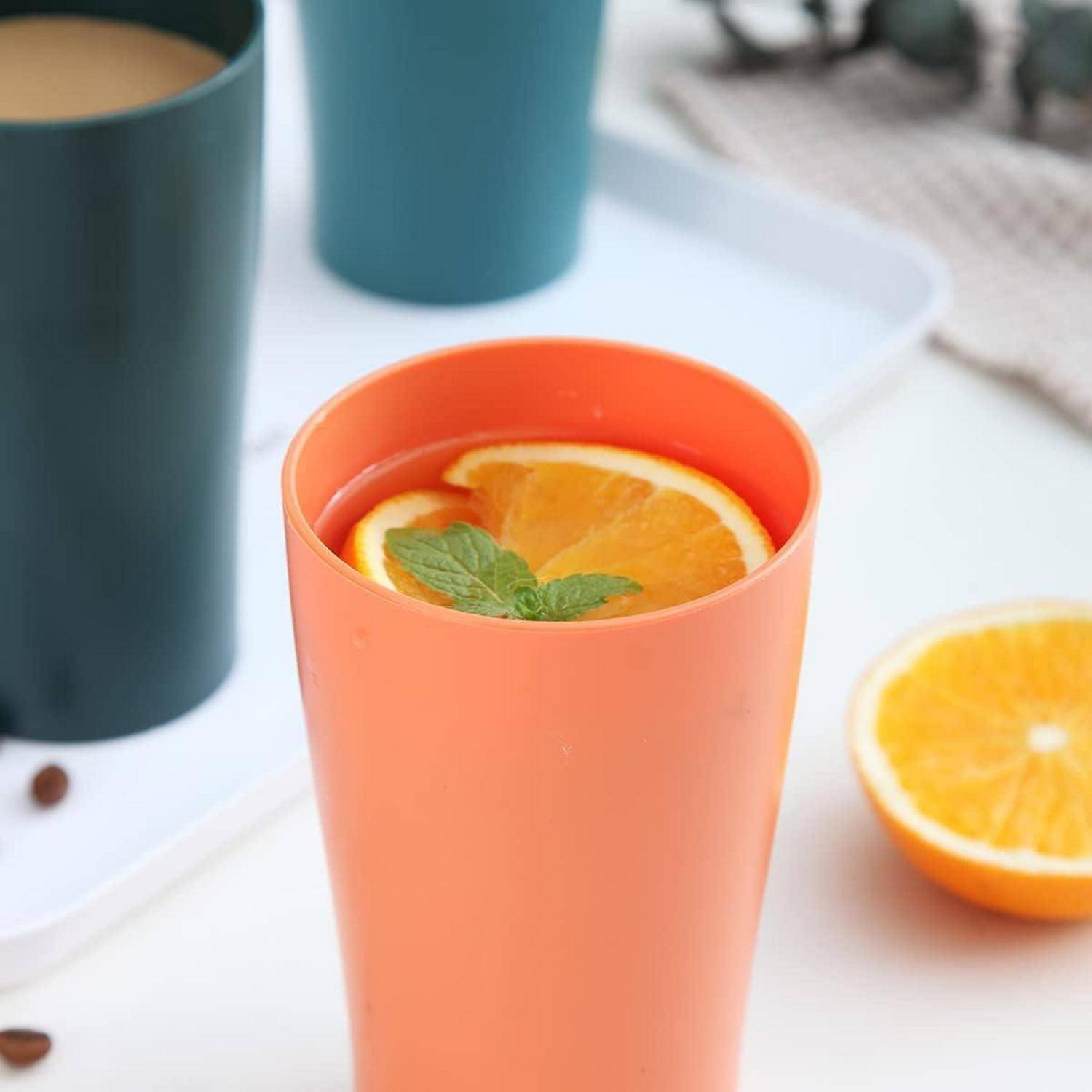 Orangenfarbene Tasse mit Orangenscheibe und Minze, neben einer grünen Tasse auf einem Tablett. Eine weitere Orangenscheibe liegt in der Nähe auf dem Tisch.