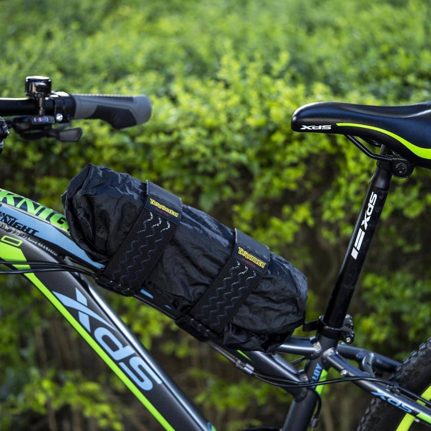 Ein Fahrrad mit einer schwarz-grünen Farbgebung, ausgestattet mit einer Satteltasche, die unter dem Sattel befestigt ist, steht vor grünen Büschen geparkt.