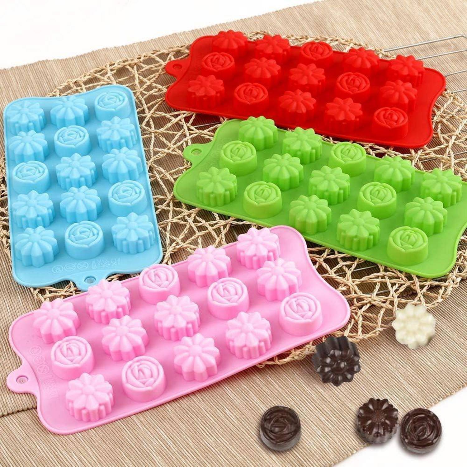 Bunte Silikonformen in Rot, Blau, Grün und Rosa auf einer Matte, geformt wie Blumen zum Backen oder für Süßigkeiten.