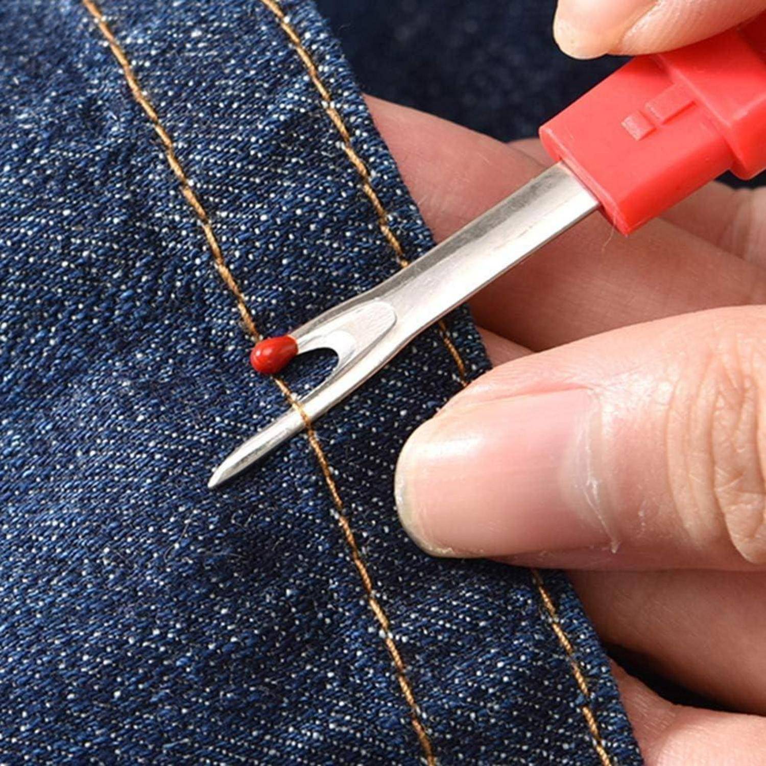 Eine Hand verwendet einen Saumtrenner, um vorsichtig einen roten Faden aus Denimstoffe zu entfernen und dabei die präzise Funktionalität des Werkzeugs zu demonstrieren.