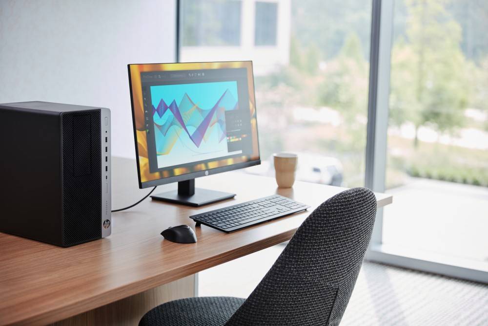 Ein Computer auf einem Schreibtisch zeigt ein buntes Diagramm mit sich kreuzenden Linien, in einer Büroumgebung mit Fensterblick.