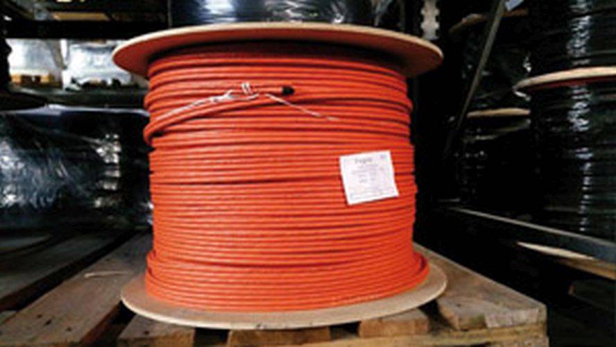 Eine große Rolle orangefarbenes Elektrokabel ist eng aufgewickelt, mit einem Etikett versehen und steht auf einer Holzpalette in einem industriellen Umfeld.