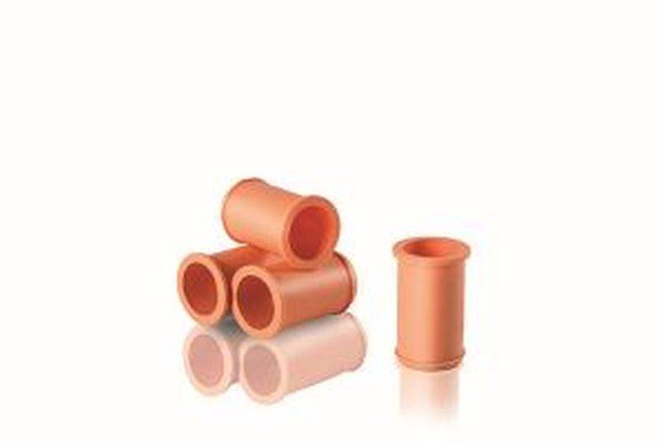 Vier gestapelte orangefarbene Rohre mit kreisförmigen Öffnungen neben einem aufrechten, die sich auf einer weißen Oberfläche spiegeln.