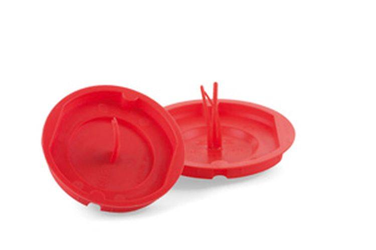 Zwei rote Plastikgeräte, von denen eines einen zentralen Dorn aufweist, sind darauf ausgelegt, Zitrusfrüchte frisch zu halten.