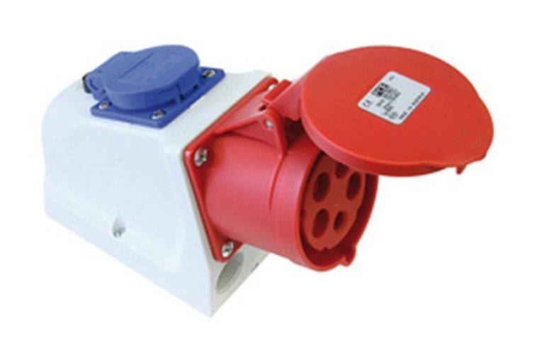 Eine rote industrielle Steckdose mit Schutzabdeckung, montiert auf einer weißen Basis, neben einer blauen Steckdose.