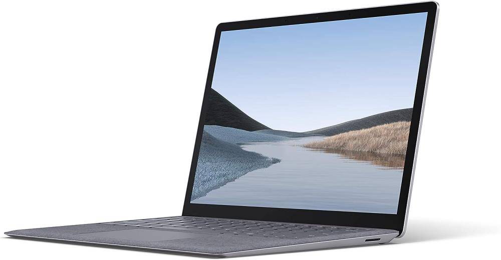 Ein Laptop mit geöffnetem Bildschirm zeigt eine friedliche Seenlandschaft mit Hügeln und einem klaren blauen Himmel, was eine ruhige und friedvolle Umgebung andeutet.