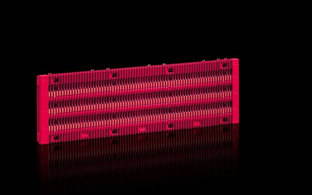 Ein langer rechteckiger roter Gegenstand mit vertikalen Rillen sitzt auf einer schwarzen reflektierenden Oberfläche und erscheint wie ein stilisiertes Kunst- oder Designobjekt.