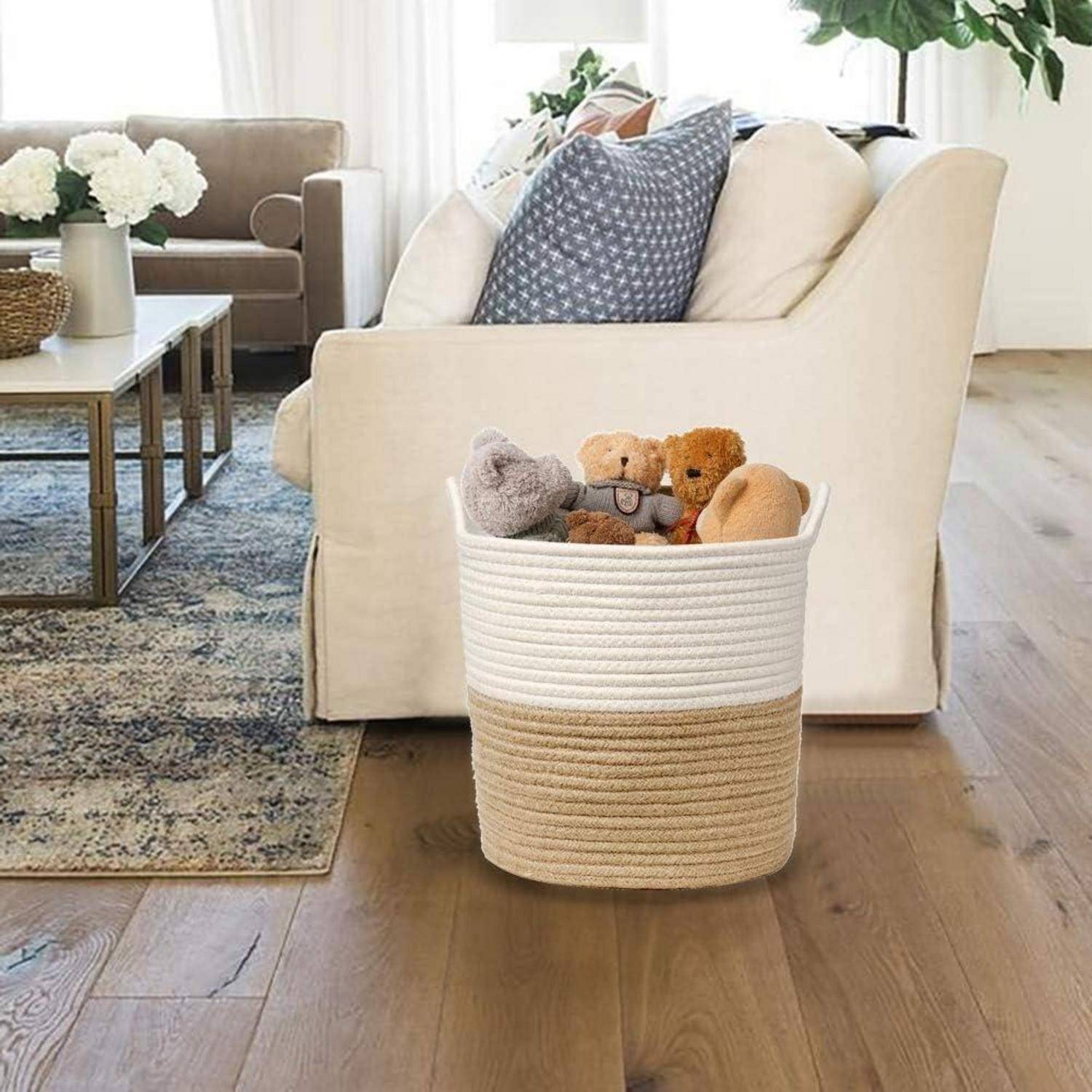 Ein gemütliches Wohnzimmer mit einem beigen Sofa, Zierkissen und einem weißen Couchtisch mit einer Vase voller Blumen. Ein Korb mit Plüschtieren steht auf dem Boden.