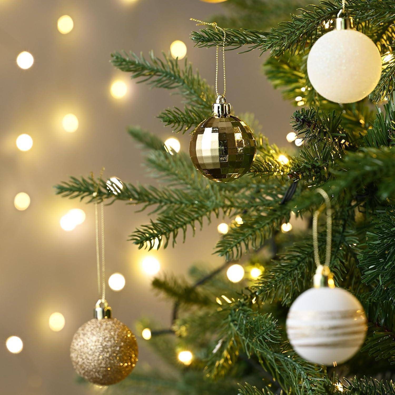 Eine Nahaufnahme eines Weihnachtsbaumes mit gold- und weißfarbenen Christbaumkugeln und funkelnden Lichtern, die eine festliche Weihnachtsstimmung vermittelt.