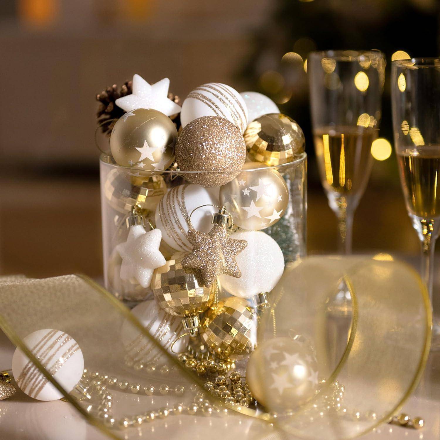 Eine klare Glasvase gefüllt mit goldenen und weißen Weihnachtskugeln, neben zwei Champagnergläsern, auf einem festlich gedeckten Tisch.