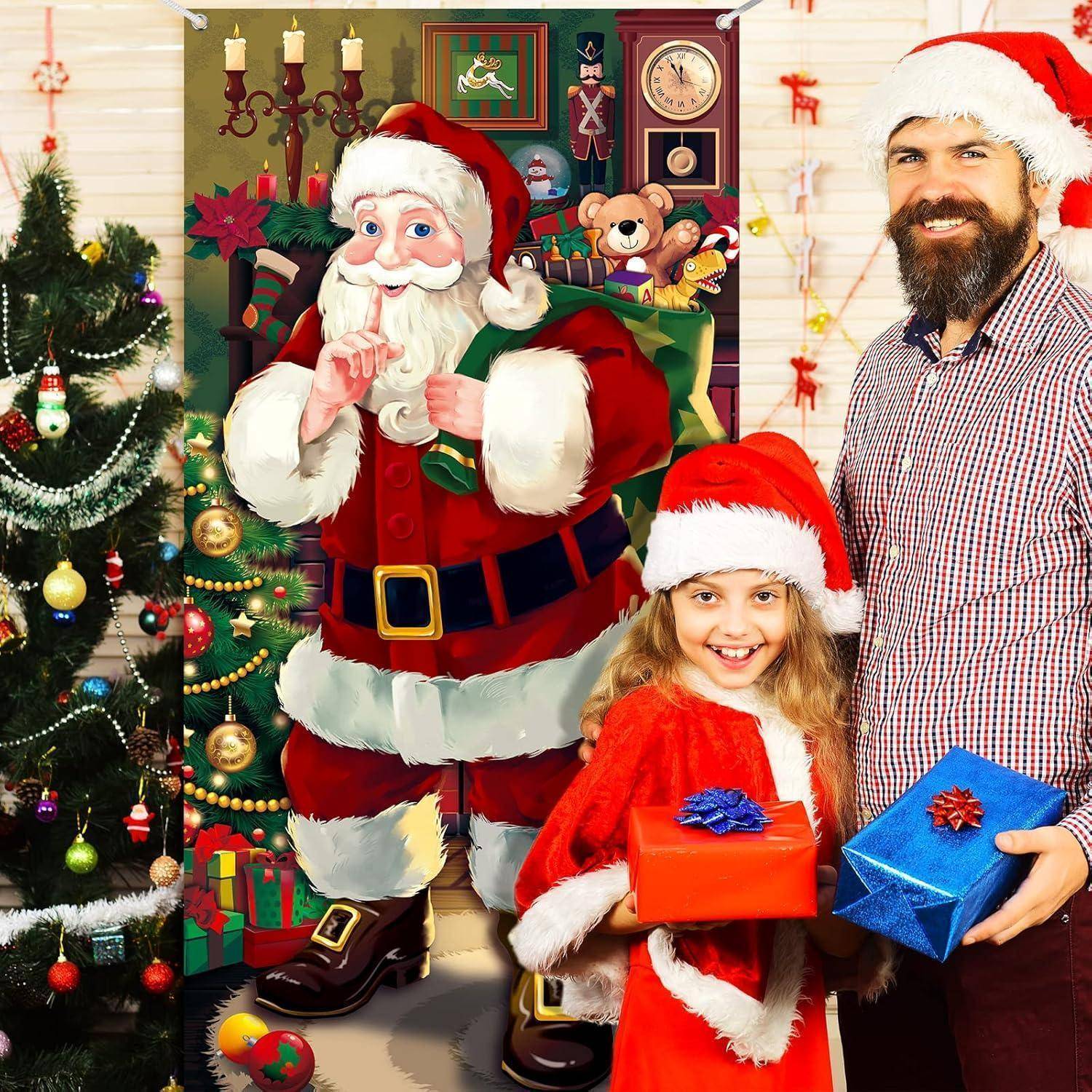 Ein Mann und ein Kind mit Weihnachtsmützen lächeln neben einer Weihnachtsausstellung mit Geschenken und einer Weihnachtsmann-Dekoration. Festliche Dekorationen und Weihnachtsschmuck sind zu sehen.