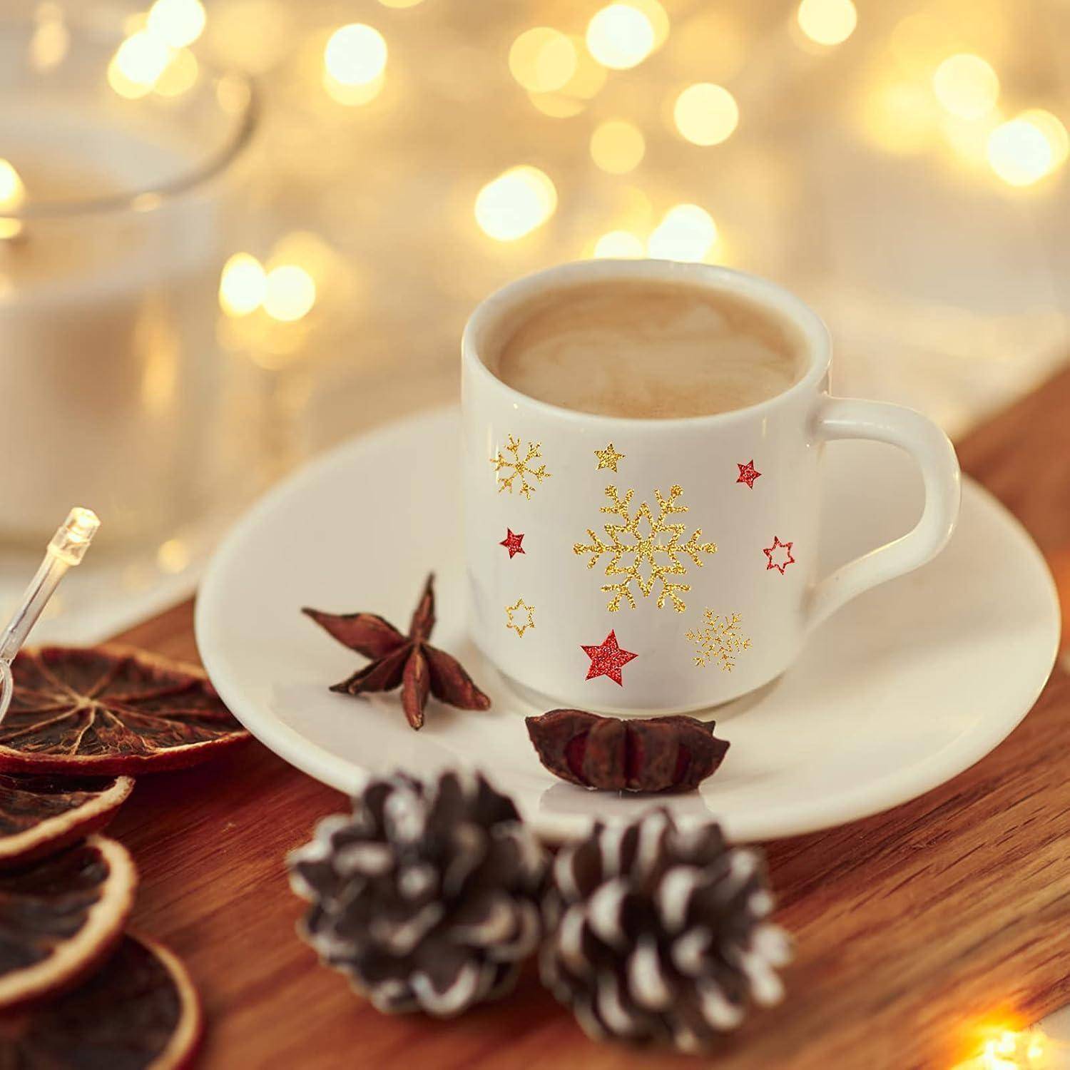 Eine festliche Kaffeetasse mit Schneeflocken- und Sternenmustern steht auf einer Untertasse. In der Nähe befinden sich getrocknete Orangen, Tannenzapfen und ein leuchtender Hintergrund.