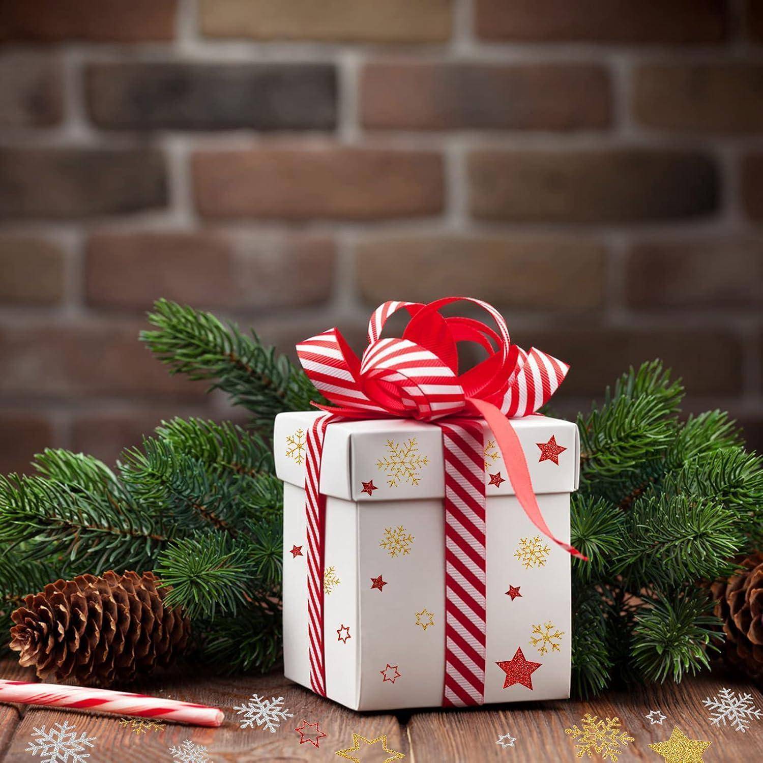 Eine festliche Geschenkbox mit Stern- und Schneeflockenmustern ist mit rotem und weißem Band umwickelt und von Tannengrün und Tannenzapfen umgeben.