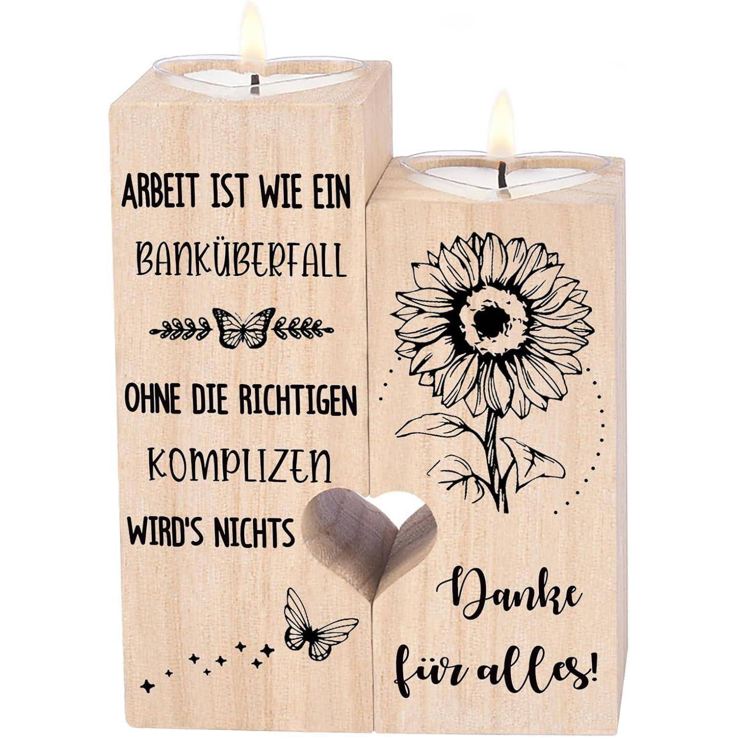 Zwei Holzkerzenhalter. Links steht der Text 'Arbeit ist wie ein Banküberfall ohne die richtigen Komplizen wird's nichts.' Rechts ist eine Sonnenblume und 'Danke für alles!' mit angezündeten Kerzen.