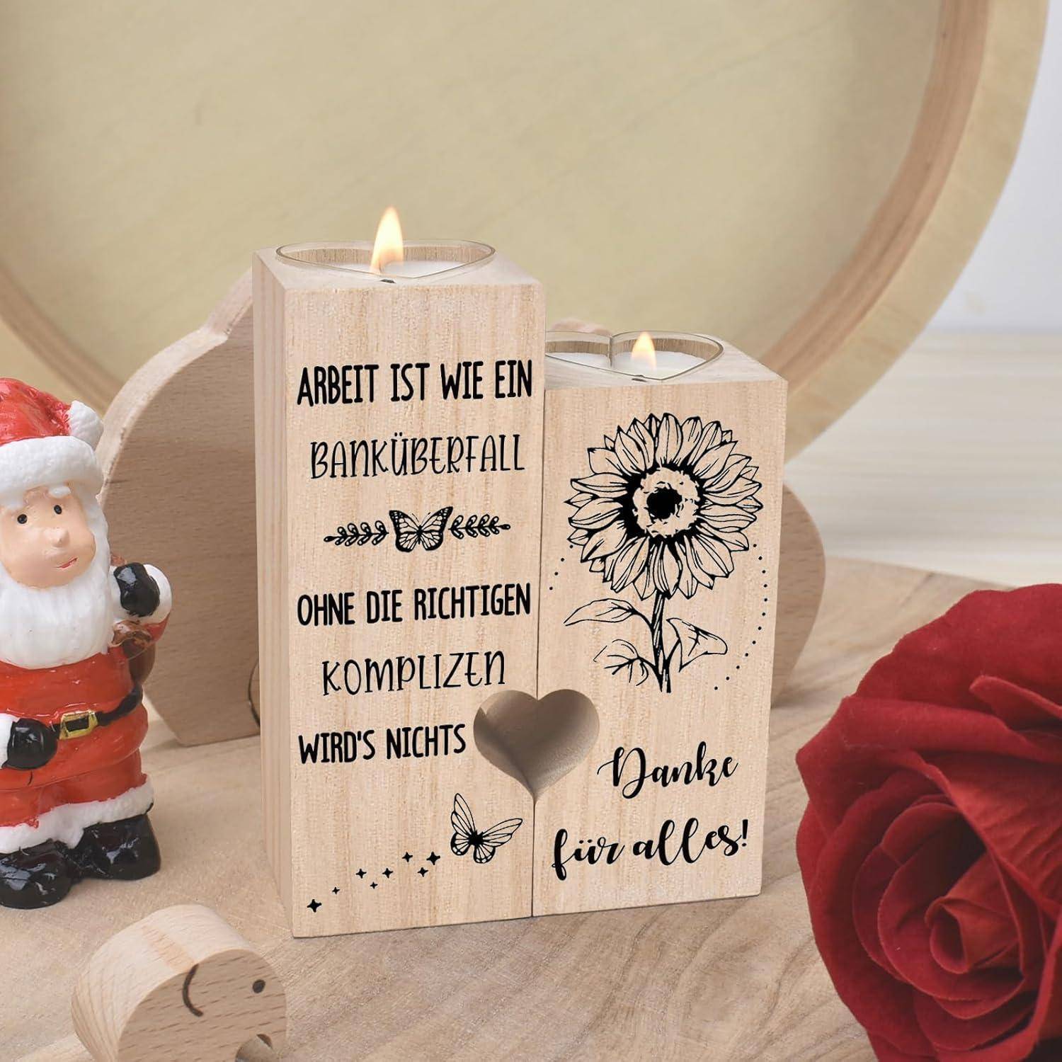 Ein Holzkerzenhalter mit zwei brennenden Kerzen zeigt gravierten Text auf Deutsch und eine Illustration einer Sonnenblume. In der Nähe steht eine Weihnachtsmann-Figur.