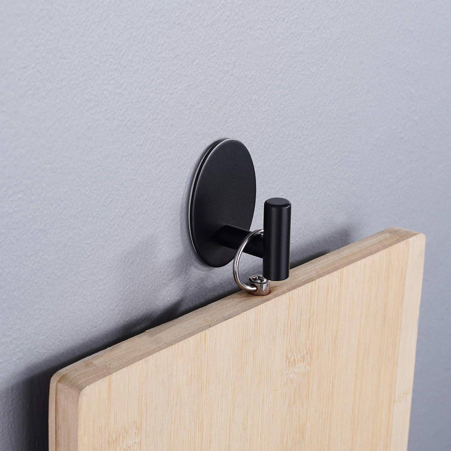 Ein Holzschneidebrett hängt an einem schlanken, runden schwarzen Wandhaken vor einem grauen Hintergrund.