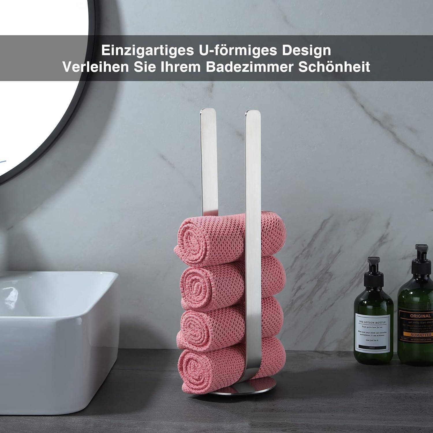 Rosa Handtücher, ordentlich aufgerollt und in einem vertikalen Metallhalter auf der Badezimmerablage gestapelt, neben einem runden Spiegel und Toilettenartikeln.