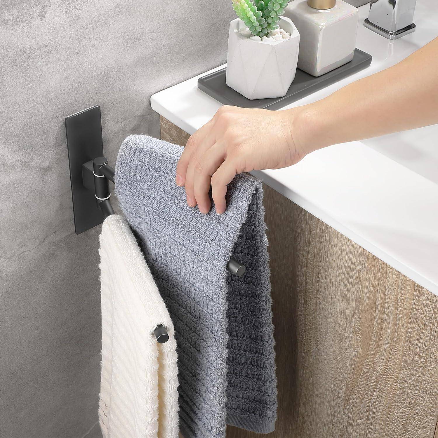 Eine Hand hängt ein strukturiertes graues Handtuch an einen Handtuchhalter an der Badezimmerwand neben einem Waschbecken mit Seifenspender und Pflanze.