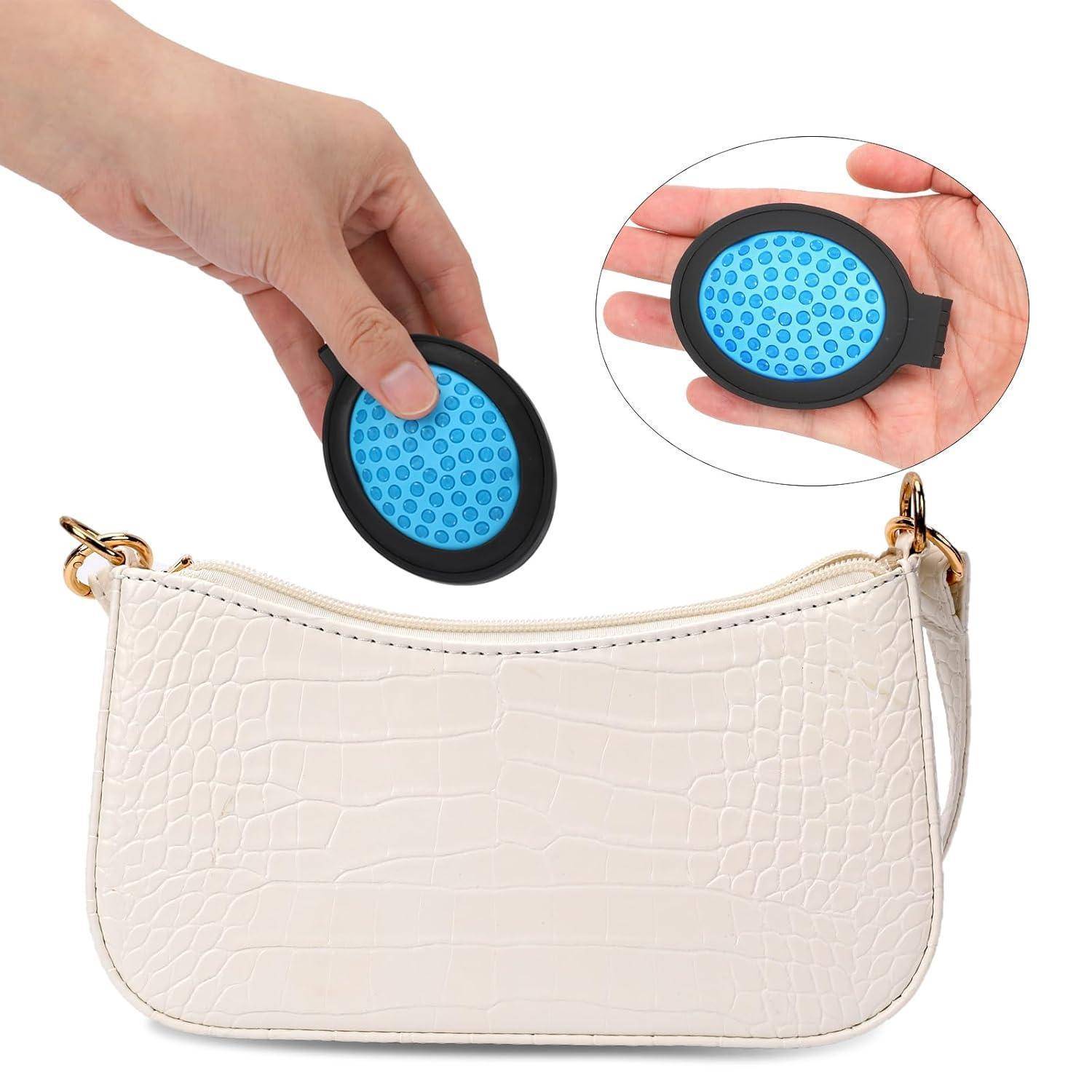 Eine weiße, krokodilgemusterte Handtasche, in die eine Hand einen scheibenförmigen blauen Organizer in eine Innentasche einschiebt und dabei die Nutzung des Stauraums betont.