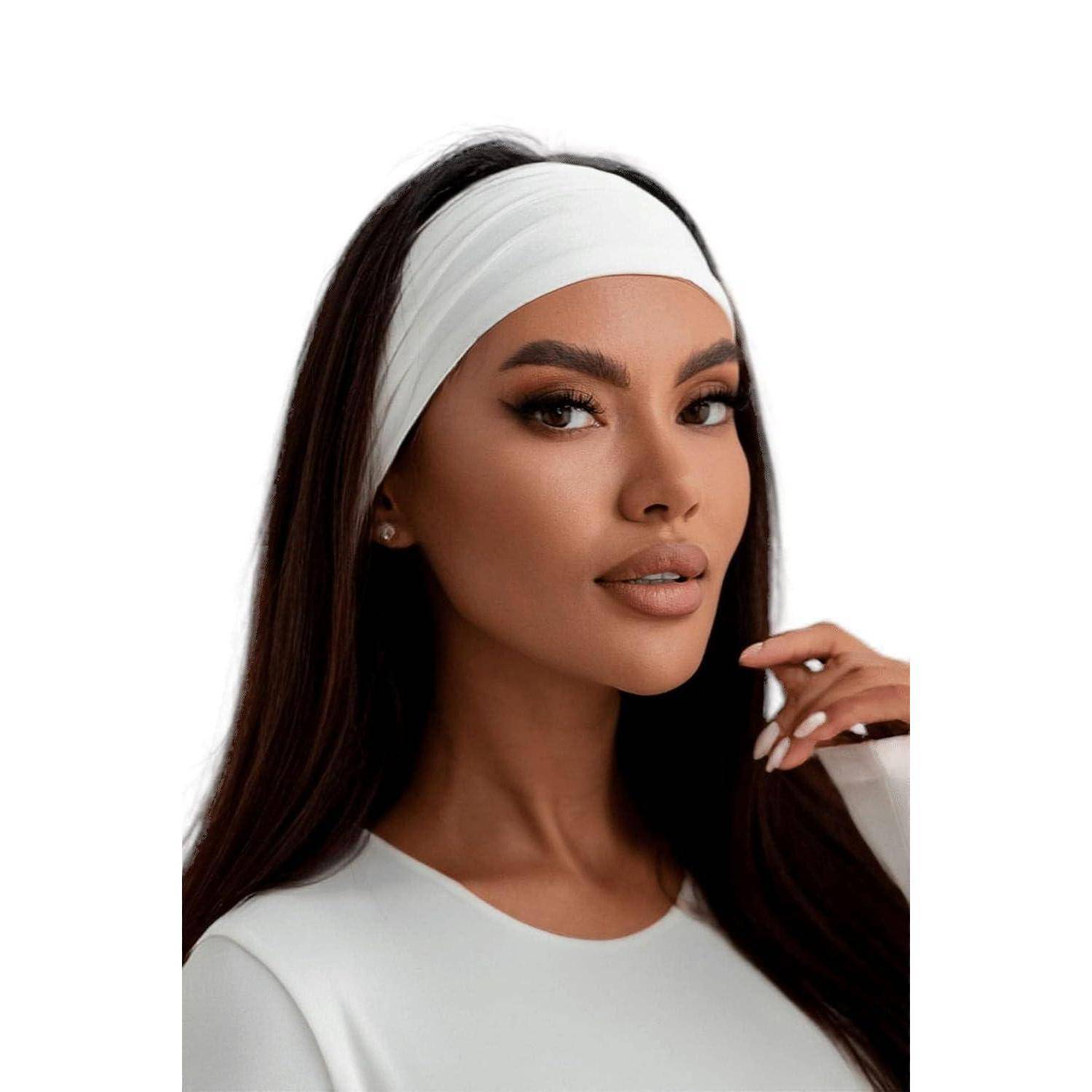 Eine Person mit langen dunklen Haaren, die ein weißes Haarband und ein weißes Oberteil trägt und selbstbewusst in die Kamera blickt, vor einem einfarbigen Hintergrund.