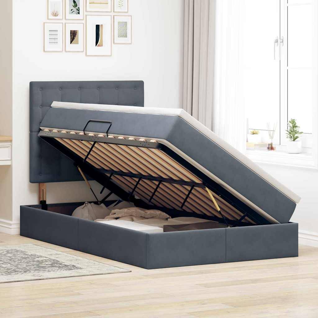 Ein grau gepolstertes Bett mit einer angehobenen Matratze offenbart Stauraum darunter. Das Zimmer hat helle Dekoration, ein Fenster und gerahmte Kunstwerke.