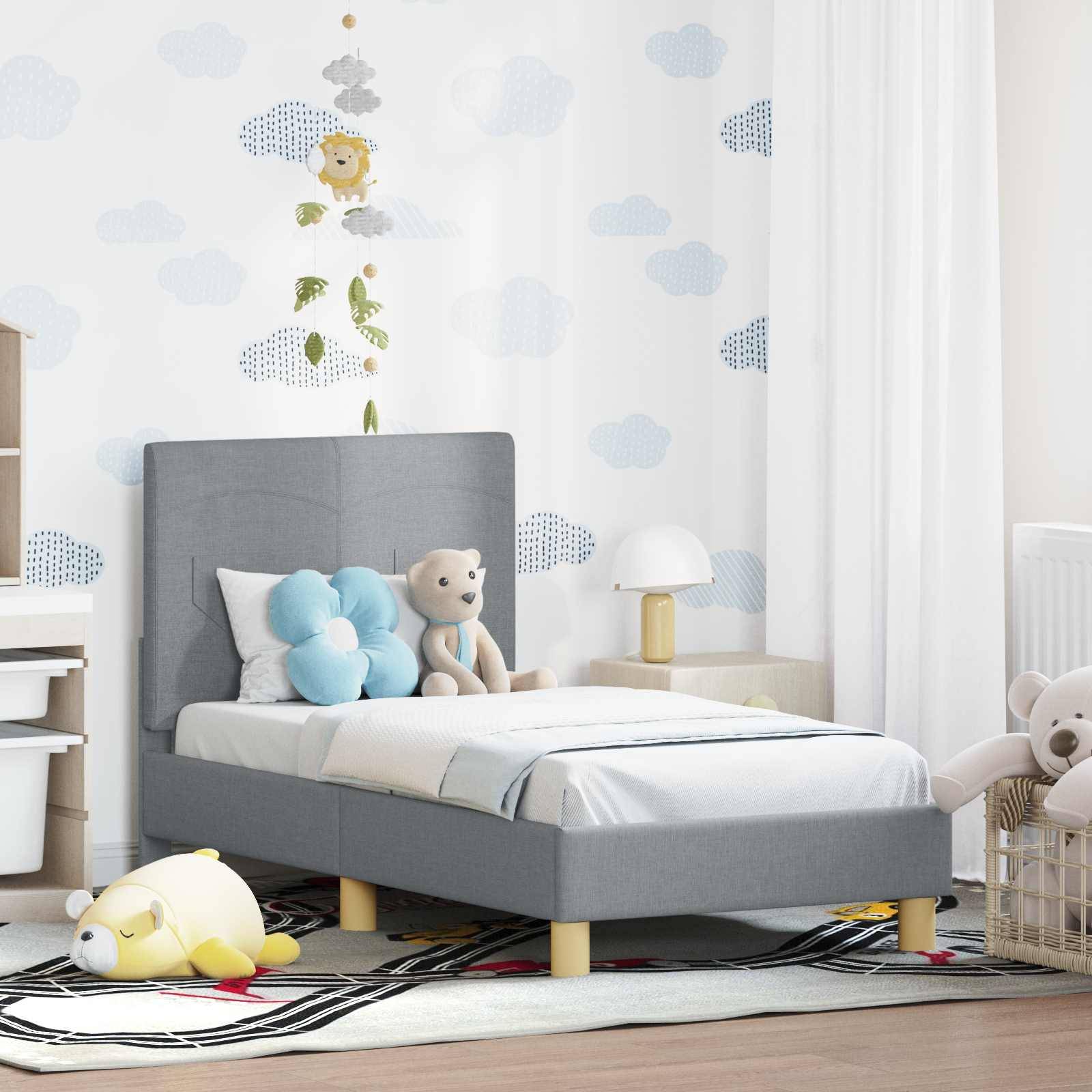 Ein Kinderzimmer mit einem grauen Bett, wolkenförmigen Kissen, Teddybären und einer Tapete mit Wolkenmuster. Ein gestreifter Teppich und ein kleiner Nachttisch vervollständigen die Einrichtung.