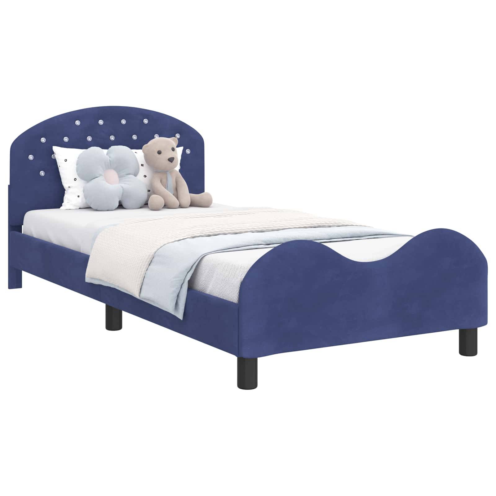 Ein Kinderbett mit einem marineblau gepolsterten Kopfteil, verziert mit kleinen klaren Juwelen, auf dem ein Plüschteddybär und ein Blumenkissen liegen.