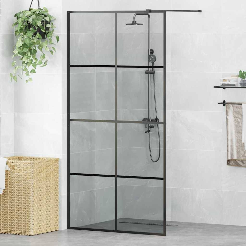 Eine moderne Dusche mit einer schwarzgerahmten Glastür und Duschkopf. Eine grüne Pflanze hängt in der Nähe, und ein Flechtkorb steht auf dem Boden.