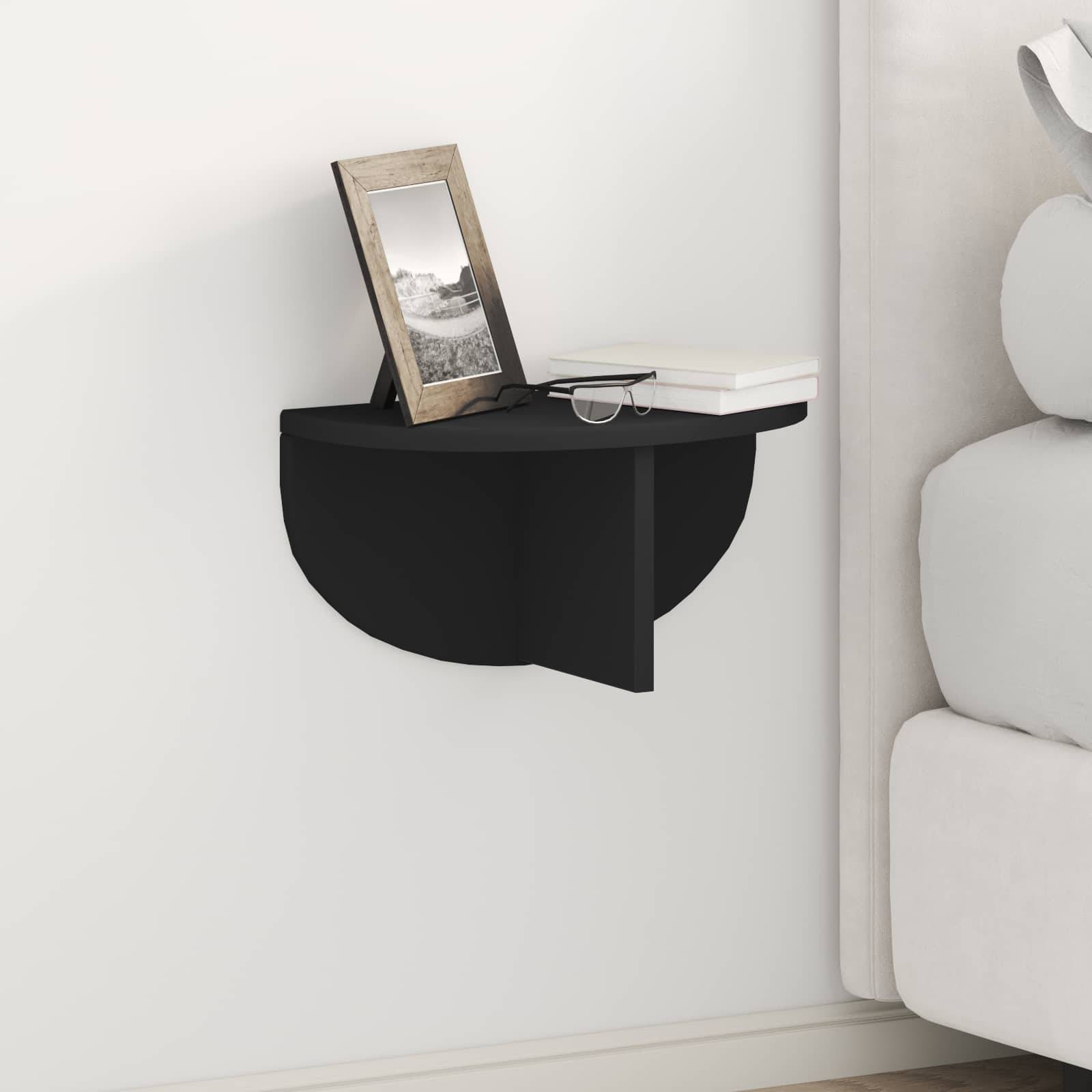 Ein kleiner schwarzer Wandtisch hält ein gerahmtes Foto und ein geschlossenes Buch neben einer hellgefärbten Couch in einem minimalistischen Raum.