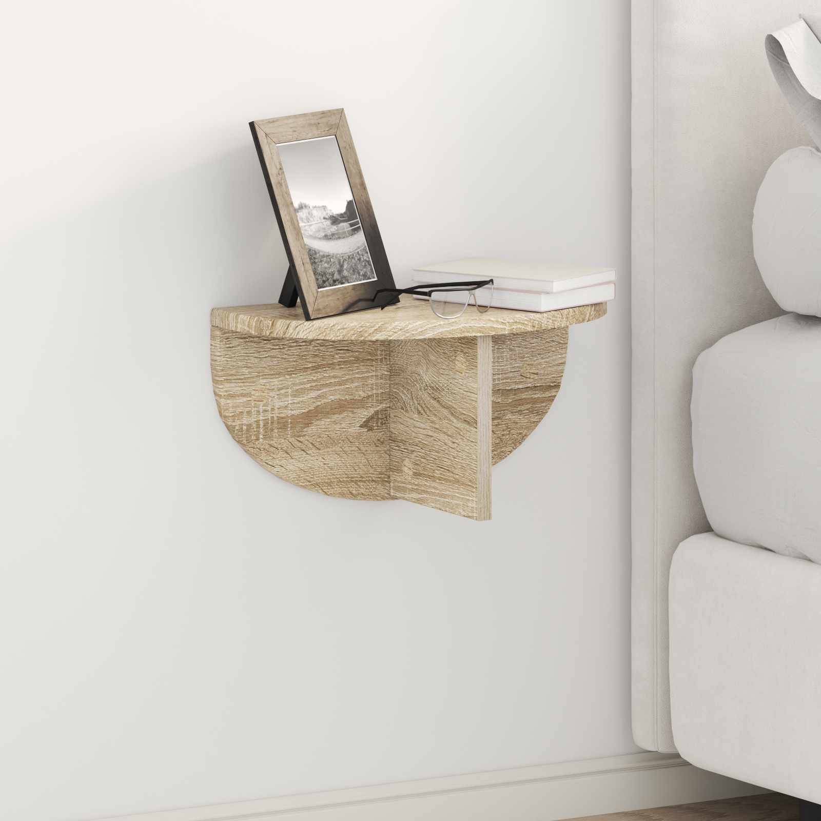 Ein kleines Holzeckregal trägt ein Buch und ein gerahmtes Foto, montiert neben einem Bett mit weißer Bettwäsche in einer minimalistischen Schlafzimmerumgebung.