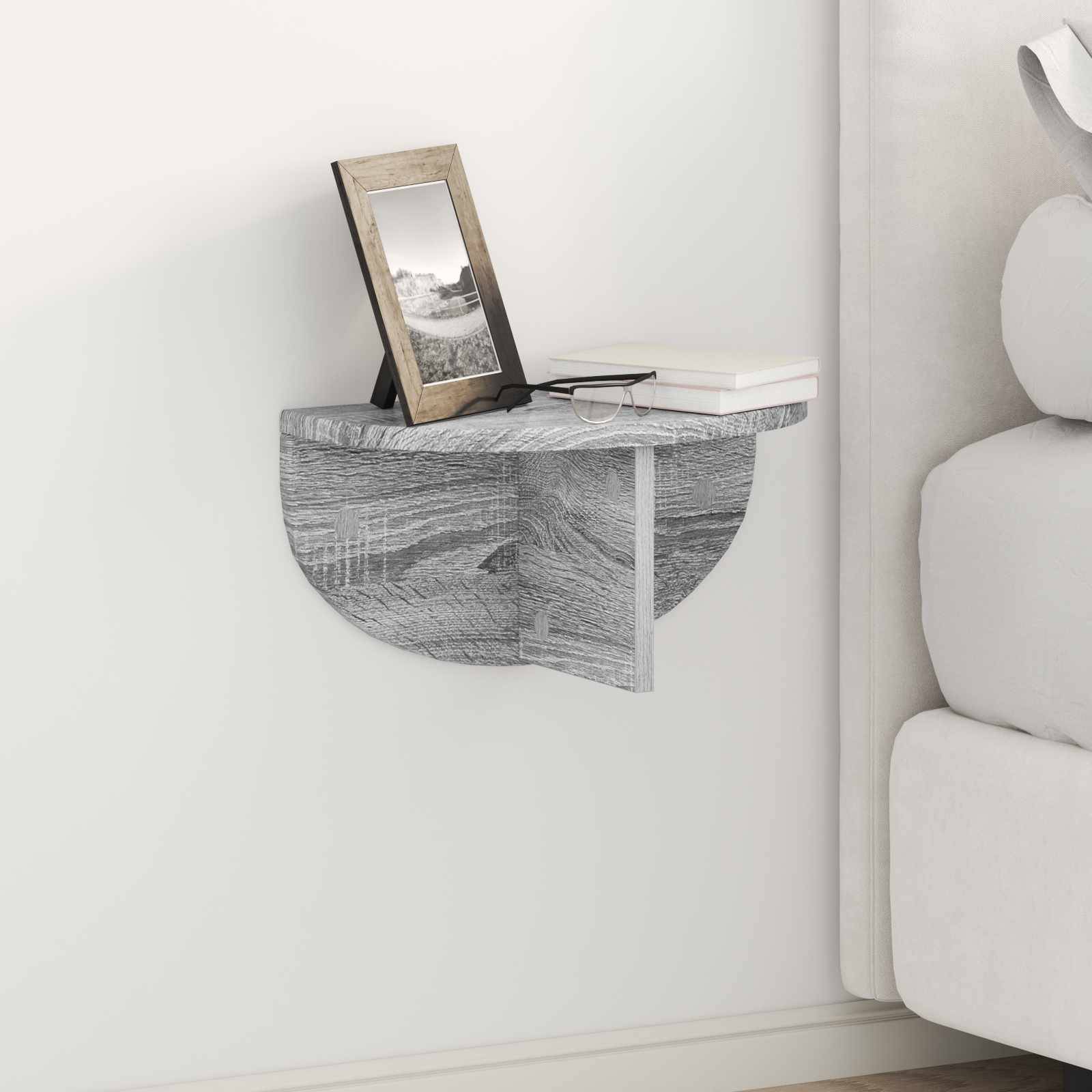 Ein kleines, halbkreisförmiges graues Wandregal mit einem gerahmten Foto und Büchern steht neben einem hellgefärbten Sofa in einem modernen Wohnzimmer.