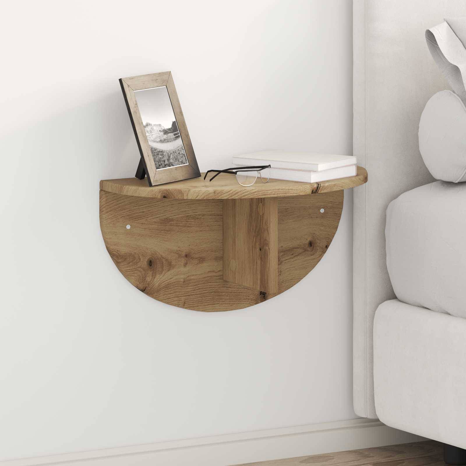 Ein kleines, halbkreisförmiges Holzwandregal hängt an der Wand und trägt einen Bilderrahmen, zwei geschlossene Bücher und ein Paar Brillen. Es befindet sich neben einem Bett.