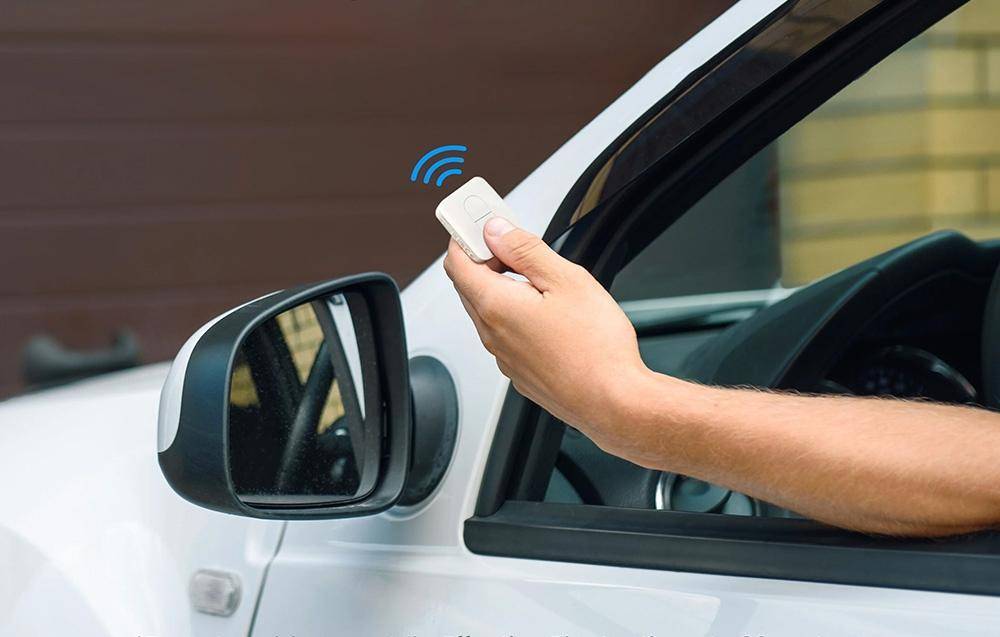 Eine Person in einem Auto verwendet eine Fernbedienung, um ein Garagentor zu öffnen, wobei die Garage im Hintergrund teilweise sichtbar ist.