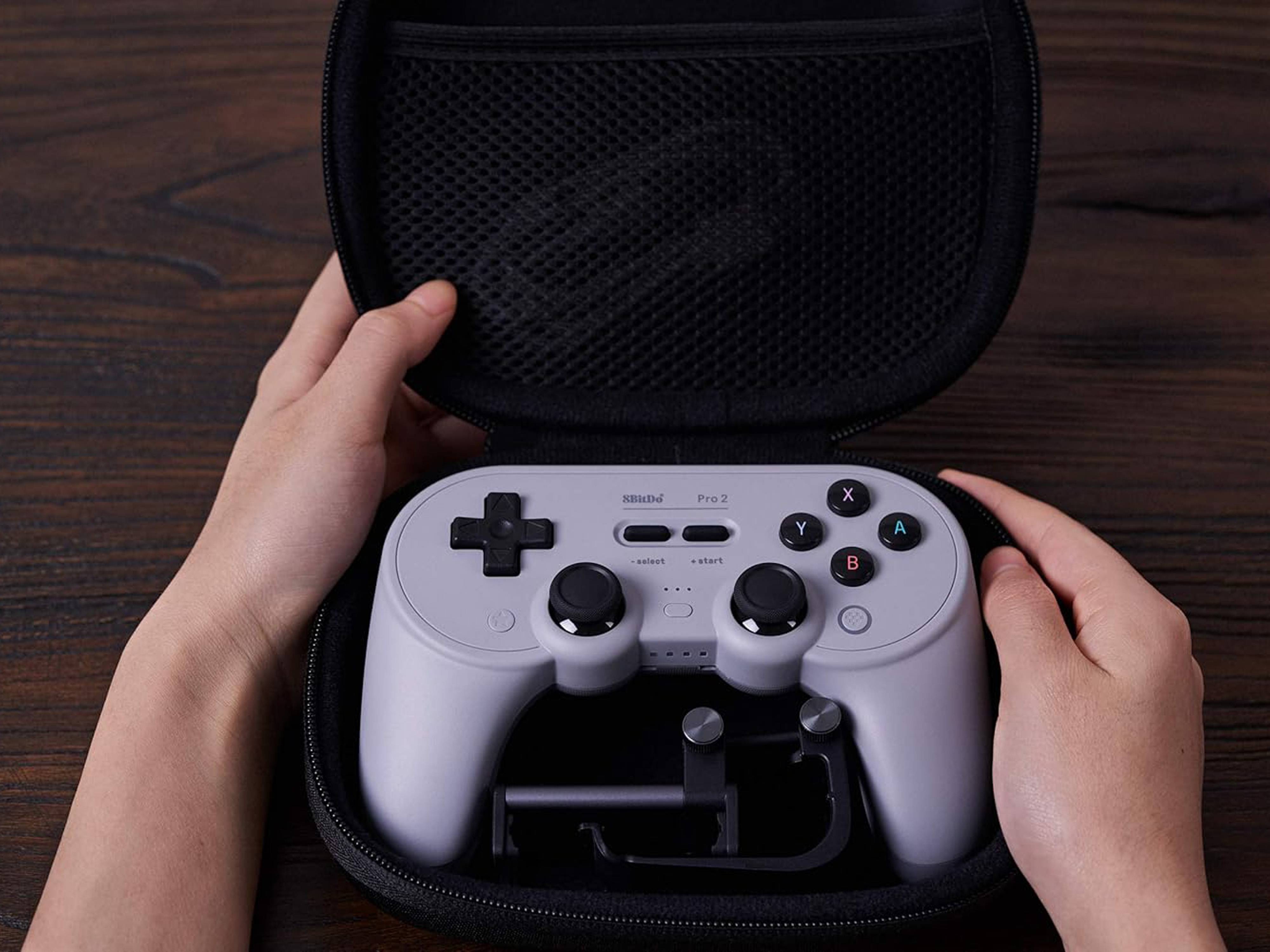 Eine Person öffnet einen schwarzen Koffer und enthüllt einen drahtlosen Gaming-Controller mit Dual-Joysticks und mehreren Tasten im Inneren, auf einer Holzoberfläche.