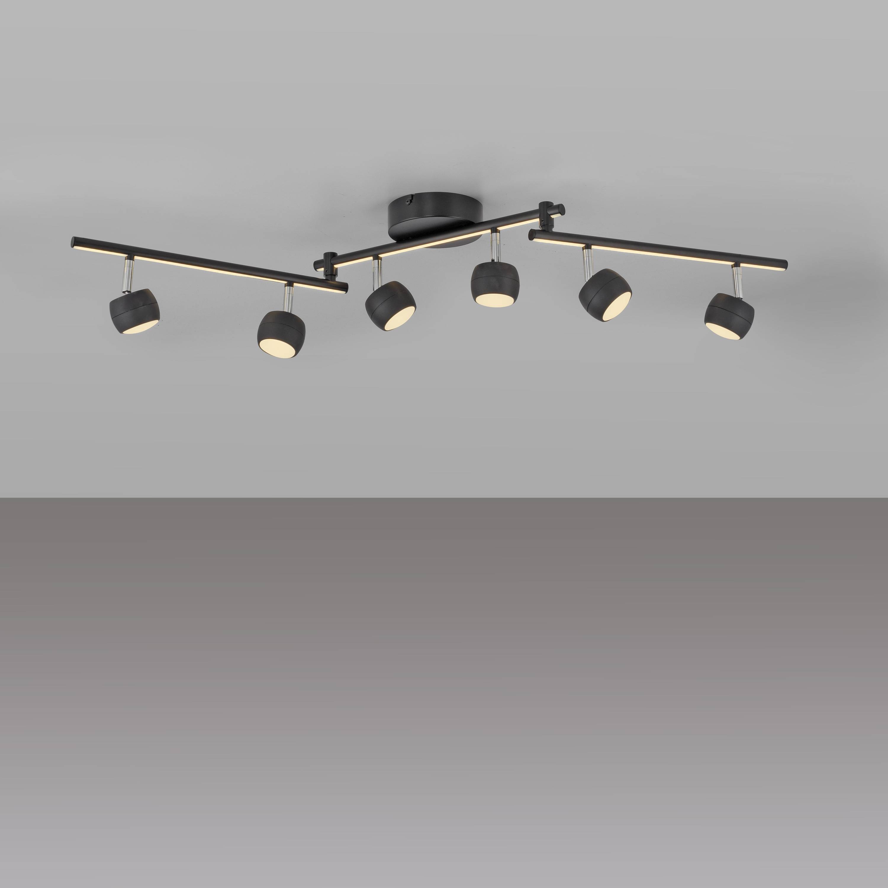 Eine an der Decke montierte Schienenlichtanlage mit sechs verstellbaren schwarzen zylindrischen Leuchten an einer silbernen Stange, vor einem grauen Hintergrund.