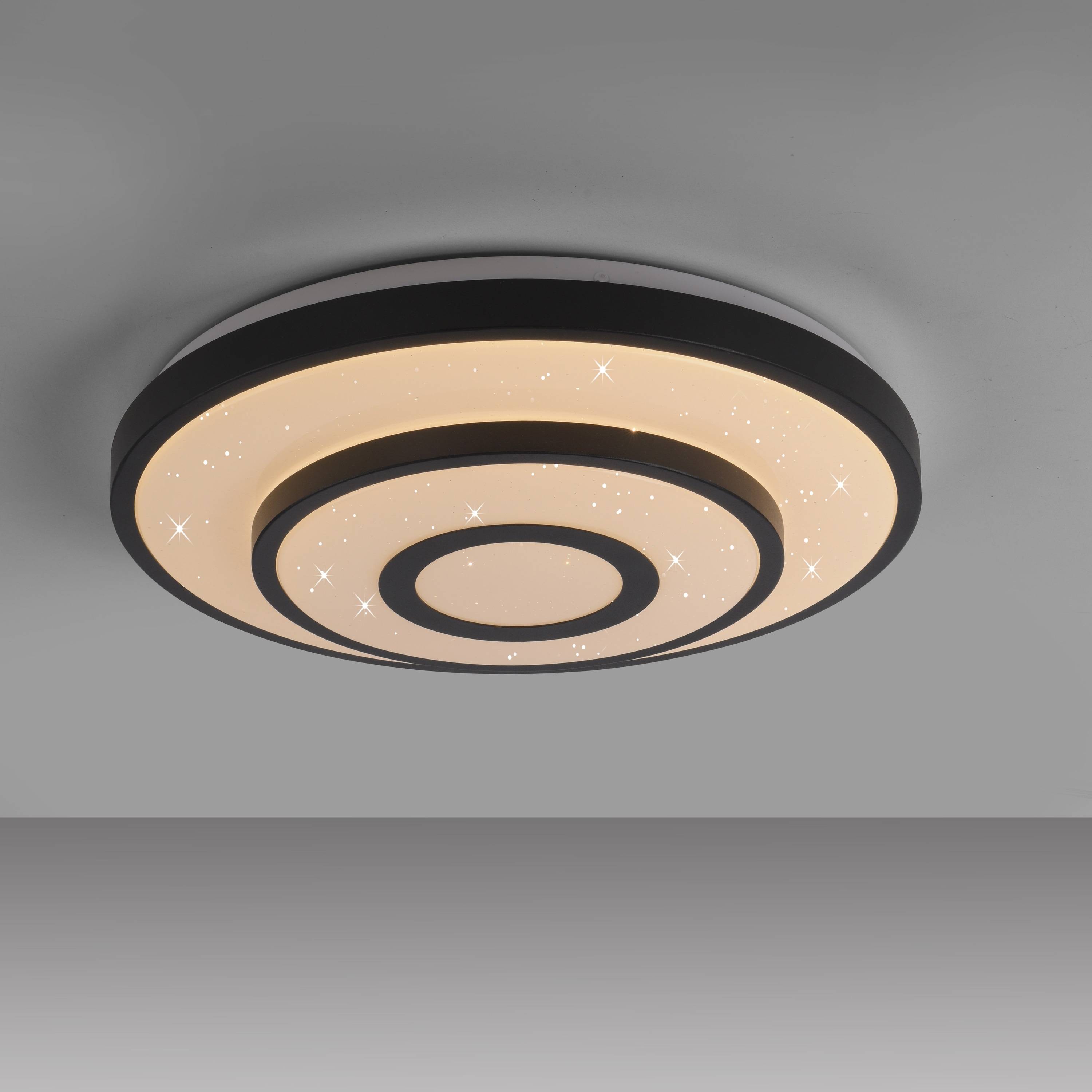 Ein modernes Deckenleuchte mit kreisförmigem Design und konzentrischen Ringen sowie einem sternenartigen Beleuchtungsmuster, vor einem einfarbigen grauen Hintergrund.
