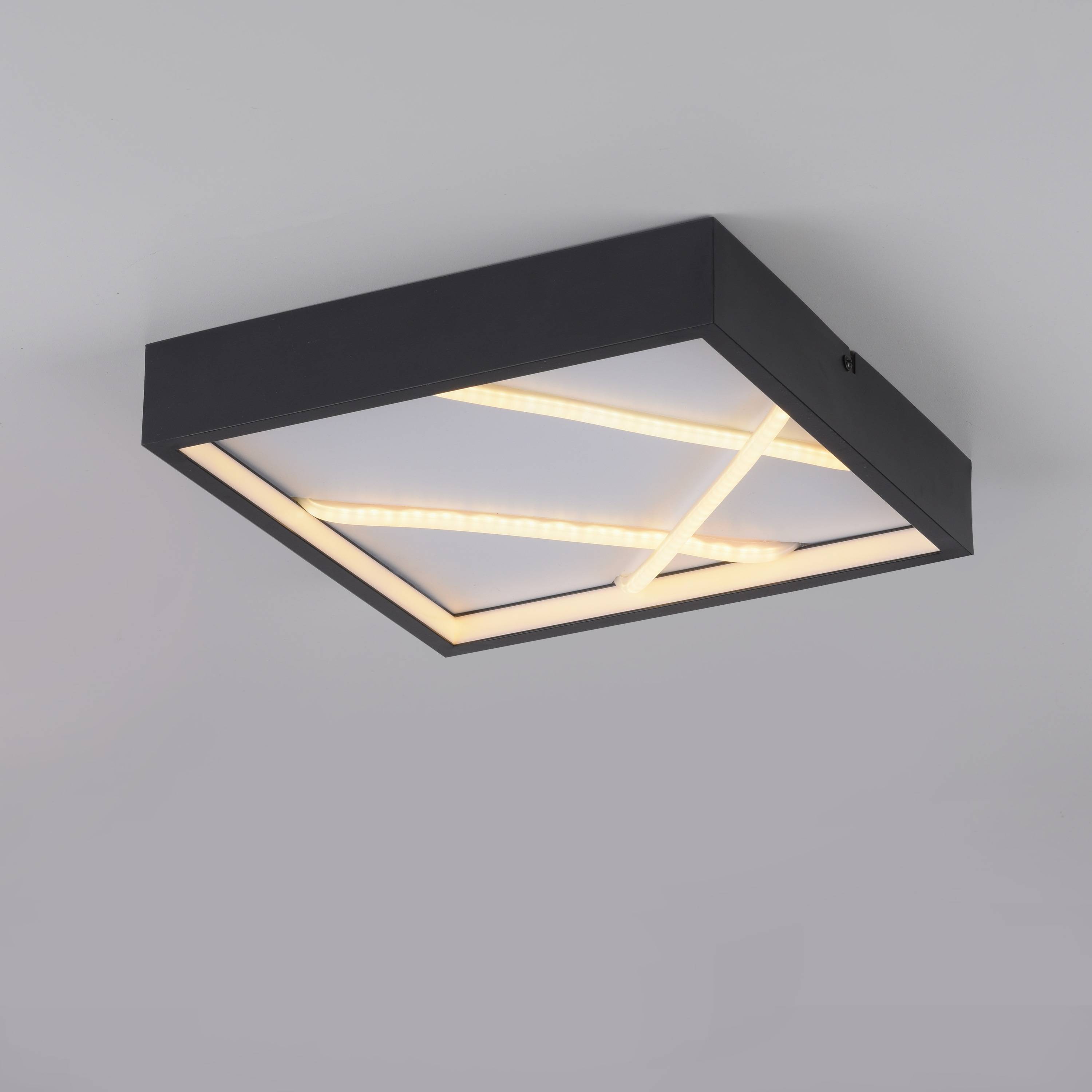 Eine moderne quadratische Deckenleuchte mit schwarzem Rahmen und sich kreuzenden LED-Streifen sorgt für Ambientelicht vor einem grauen Deckengrund.