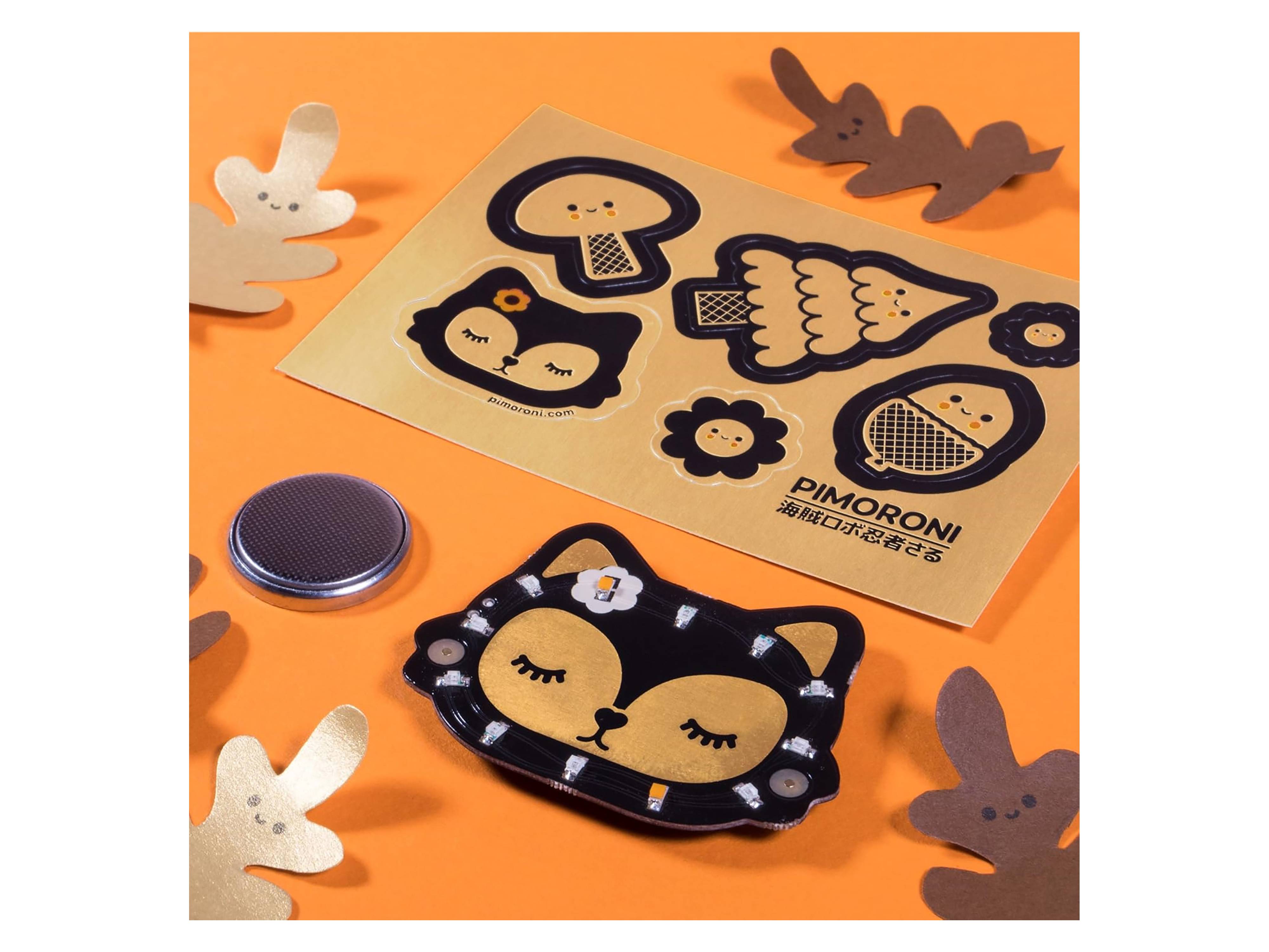 Stickerbogen mit verschiedenen schwarzen Katzendesigns und -formen auf orangefarbenem Hintergrund mit dekorativen Goldblattakzenten in der Nähe.