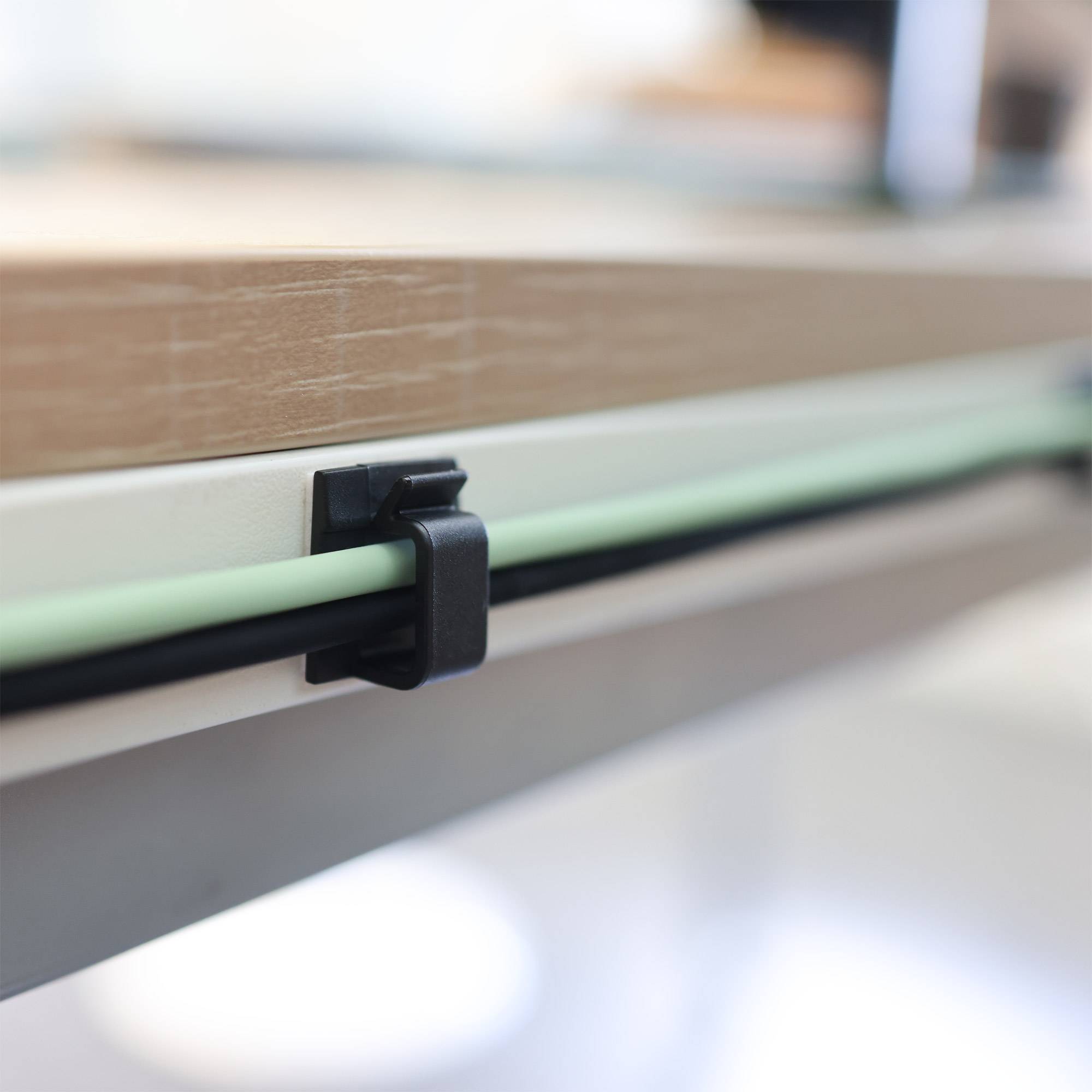 Eine Nahaufnahme des Randes eines Schreibtischs, die Kabelführungsclips zeigt, die Kabel ordentlich darunter befestigen.