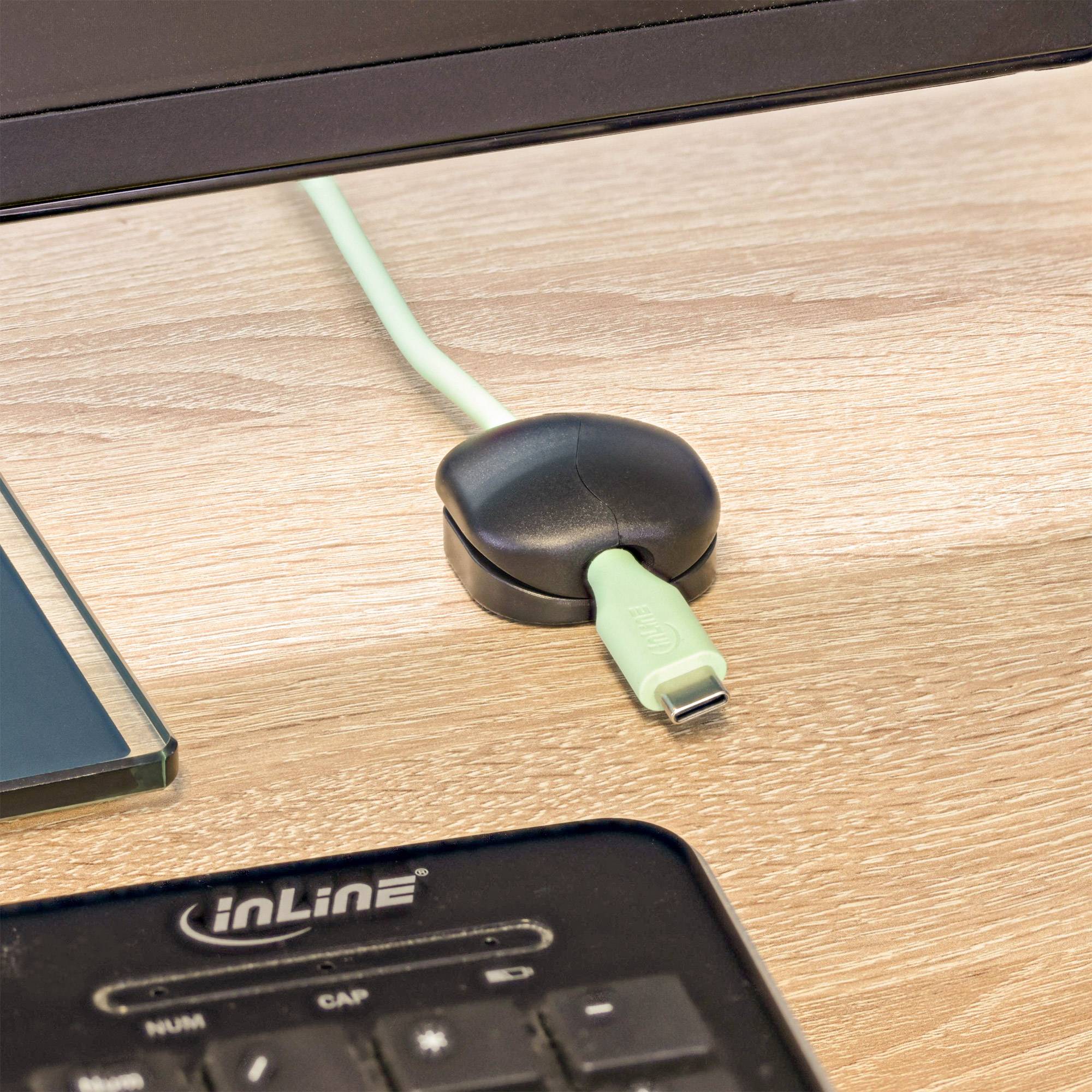 Ein hellgrünes USB-Kabel ist teilweise in einen schwarzen Dock auf einem Holzschreibtisch eingesteckt, wobei eine Tastatur im Vordergrund sichtbar ist.
