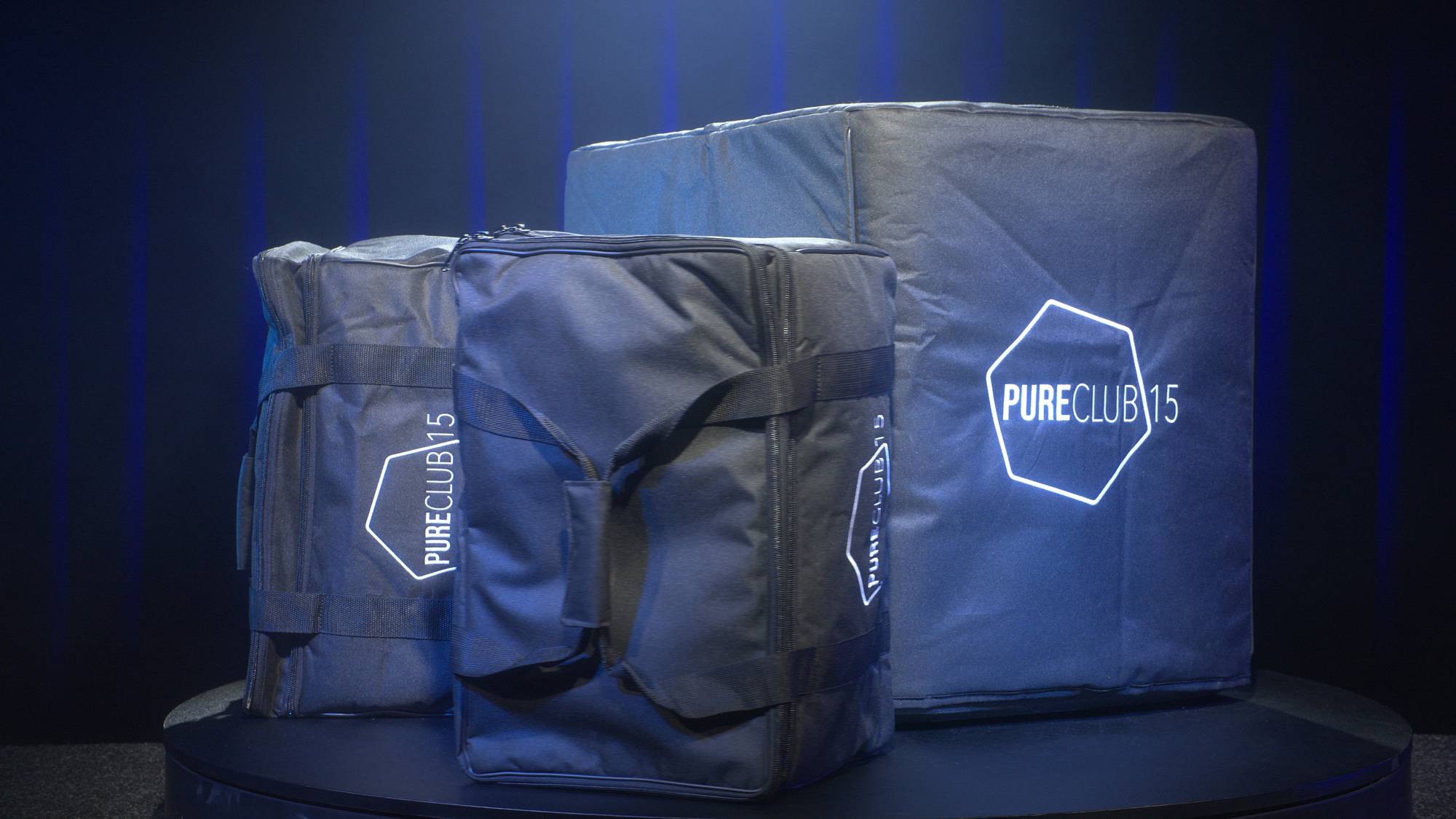 Drei schwarze Taschen mit dem Logo 'PURE CLUB 15' und 'PURE CLUB' in einer blau beleuchteten Umgebung, möglicherweise zur Lagerung oder zum Transport verwendet.