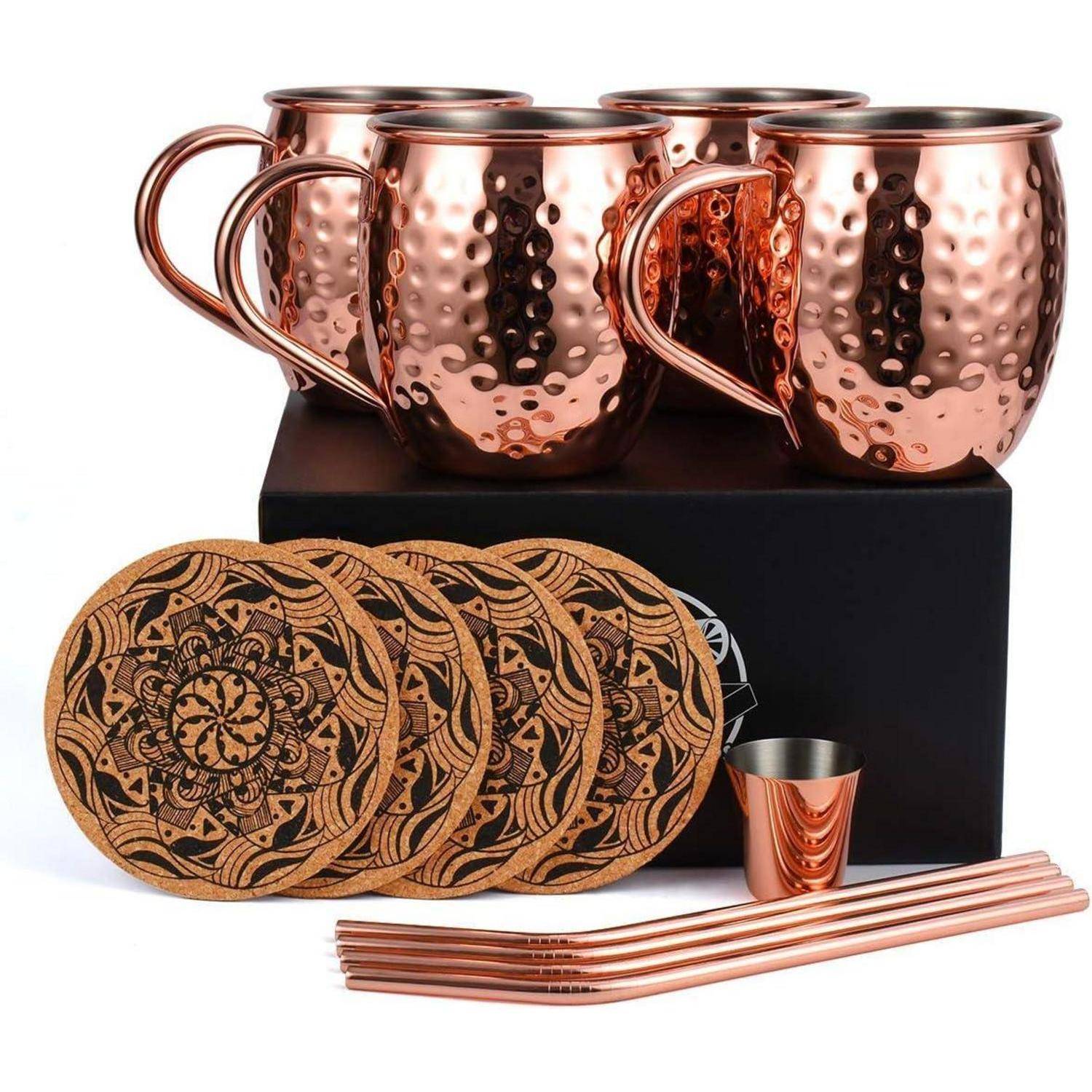 Ein Set aus vier Kupferbechern mit gehämmerter Oberfläche, sechs kunstvoll gestalteten Untersetzen und vier Kupferstrohhalmen, angeordnet auf einer schwarzen Box.