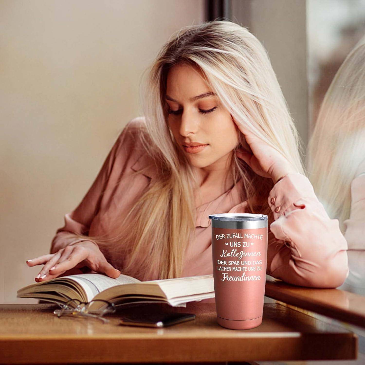 Eine Frau in einem pinken Outfit liest ein Buch an einem Tisch mit einer pinken Tasse.