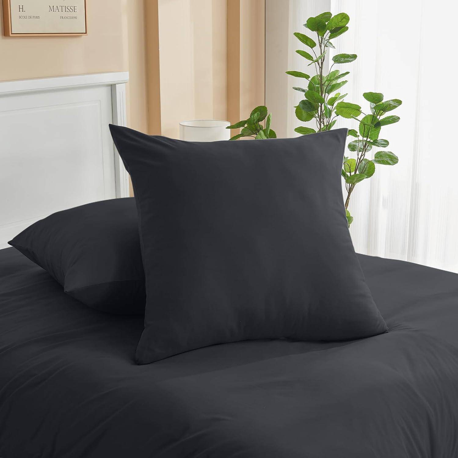 Ein ordentlich gemachtes Bett mit dunkelgrauer Bettwäsche, großen quadratischen Kissen und einer hohen grünen Pflanze daneben schafft eine ruhige Schlafzimmeratmosphäre.