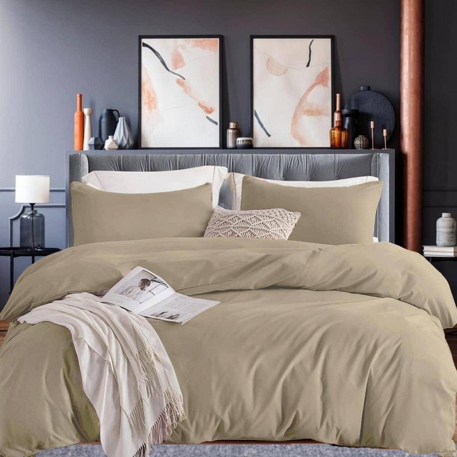 Ein ordentlich gemachtes Bett in einem stilvollen Schlafzimmer ist mit beige Bettwäsche und Zierkissen ausgestattet. Abstrakte Kunst hängt über dem Kopfende und schafft eine friedliche Atmosphäre.
