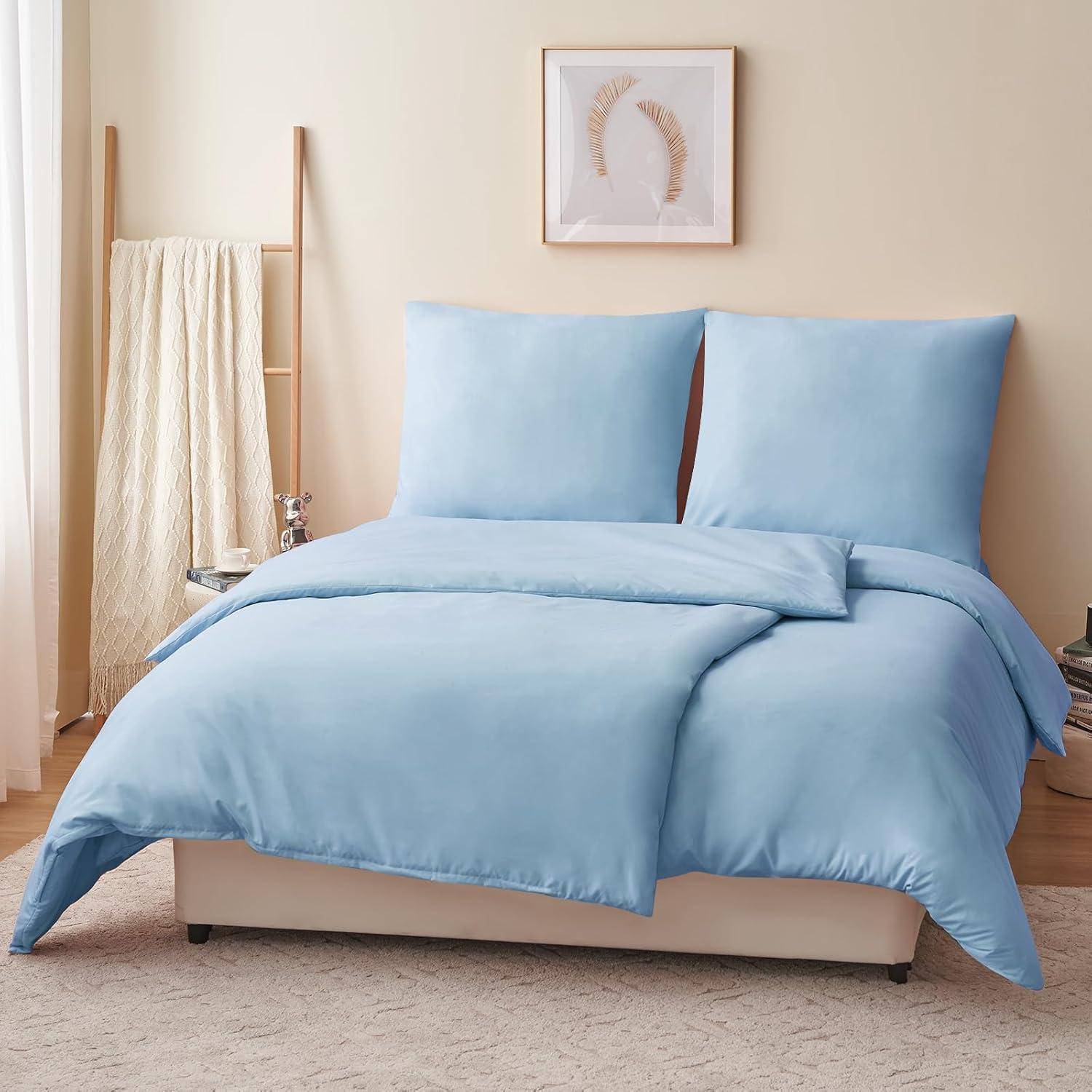 Ein ordentlich hergerichtetes Bett mit weicher blauer Bettwäsche, vor einer hellgefärbten Wand mit minimalistischer Dekoration. Eine gemütliche und friedliche Schlafzimmerszene.