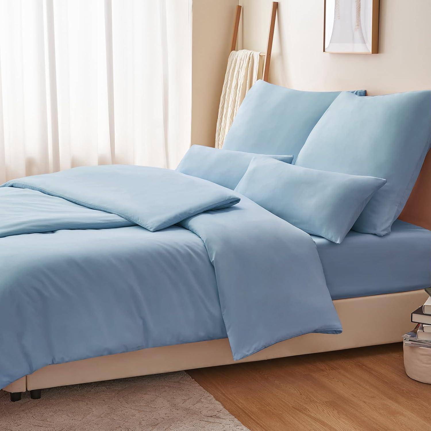 Ein ordentlich gemachtes Bett mit hellblauen Betttüchern und flauschigen Kissen, neben einem kleinen beigen Teppich auf Holzboden in einem Raum mit sanftem natürlichem Licht.