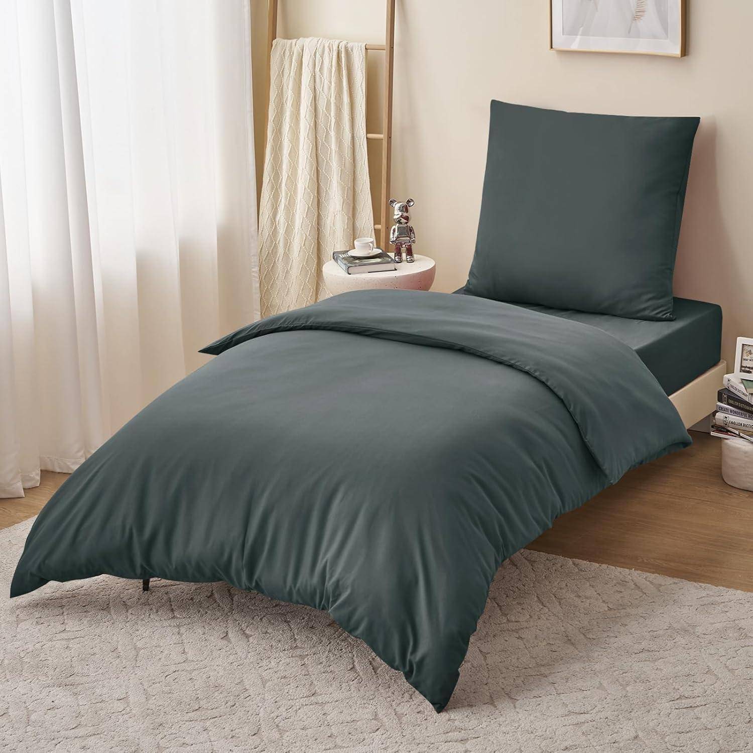 Ein ordentlich gemachtes Bett mit dunkelgrauer Bettwäsche, vor einem sanften Hintergrund, neben einer kleinen Holzleiter, die ein Handtuch und Dekorationsgegenstände auf einem Regal trägt.