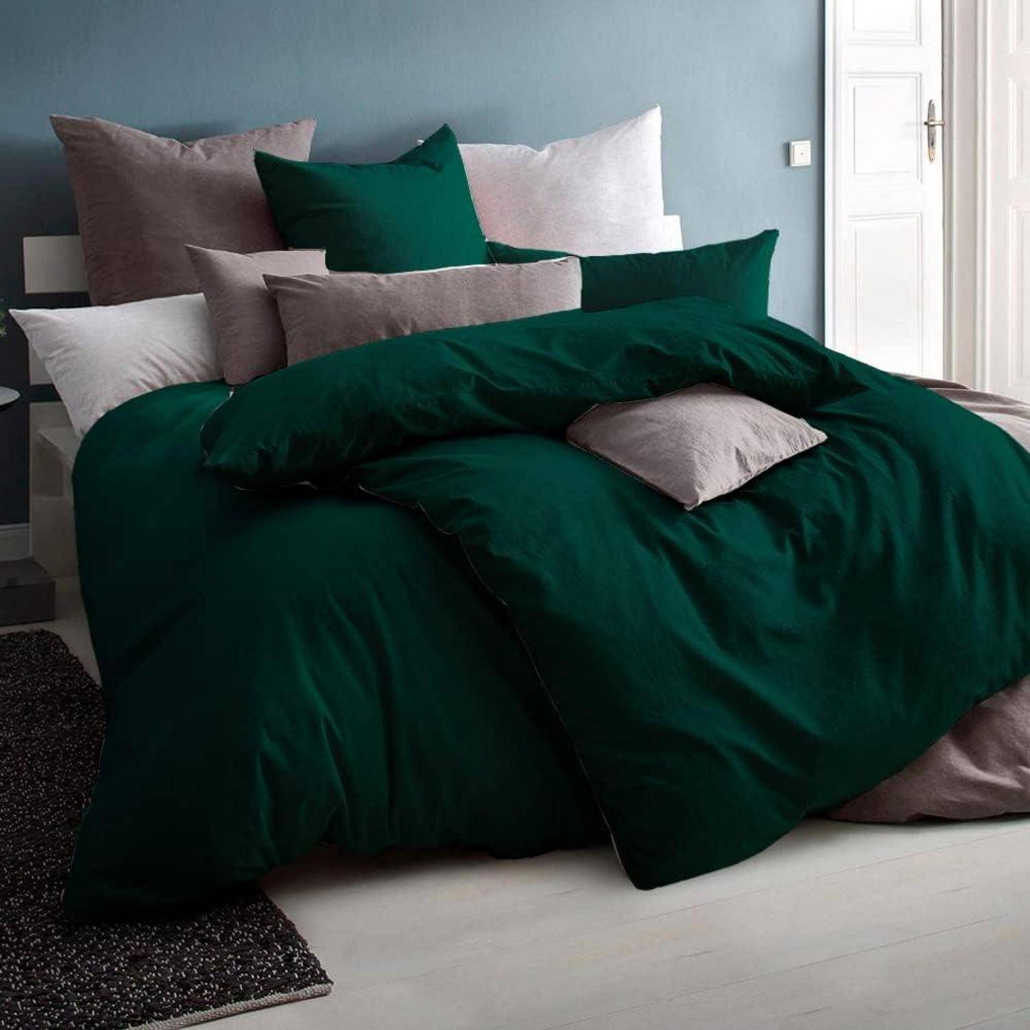 Ein ordentlich gemachtes Bett mit mehreren grünen und grauen Kissen und einer dunkelgrünen Bettdecke in einem modernen Schlafzimmerambiente.